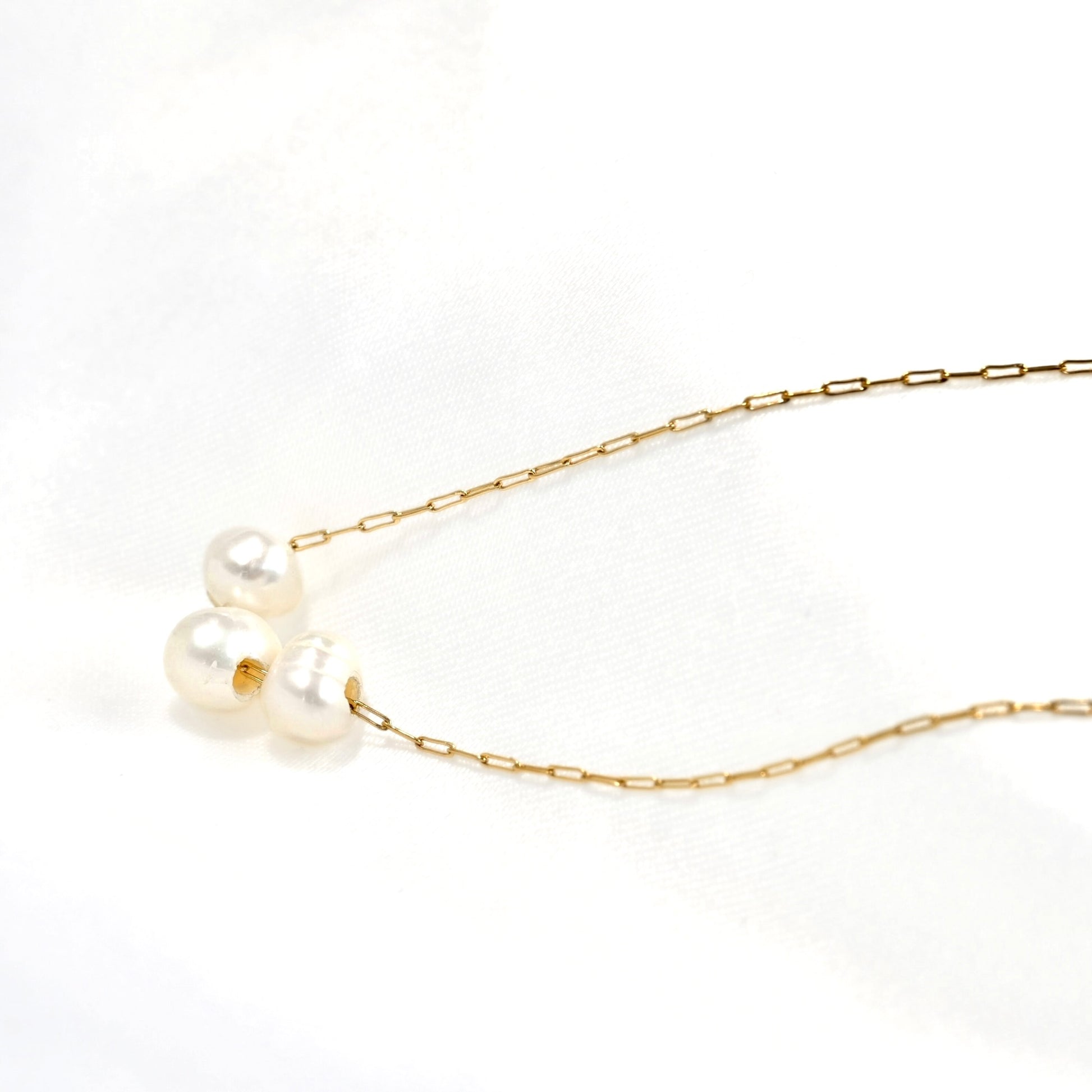 A delicate gold chain necklace featuring three small white baroque pearls clustered on one end, displayed on a clean white background.