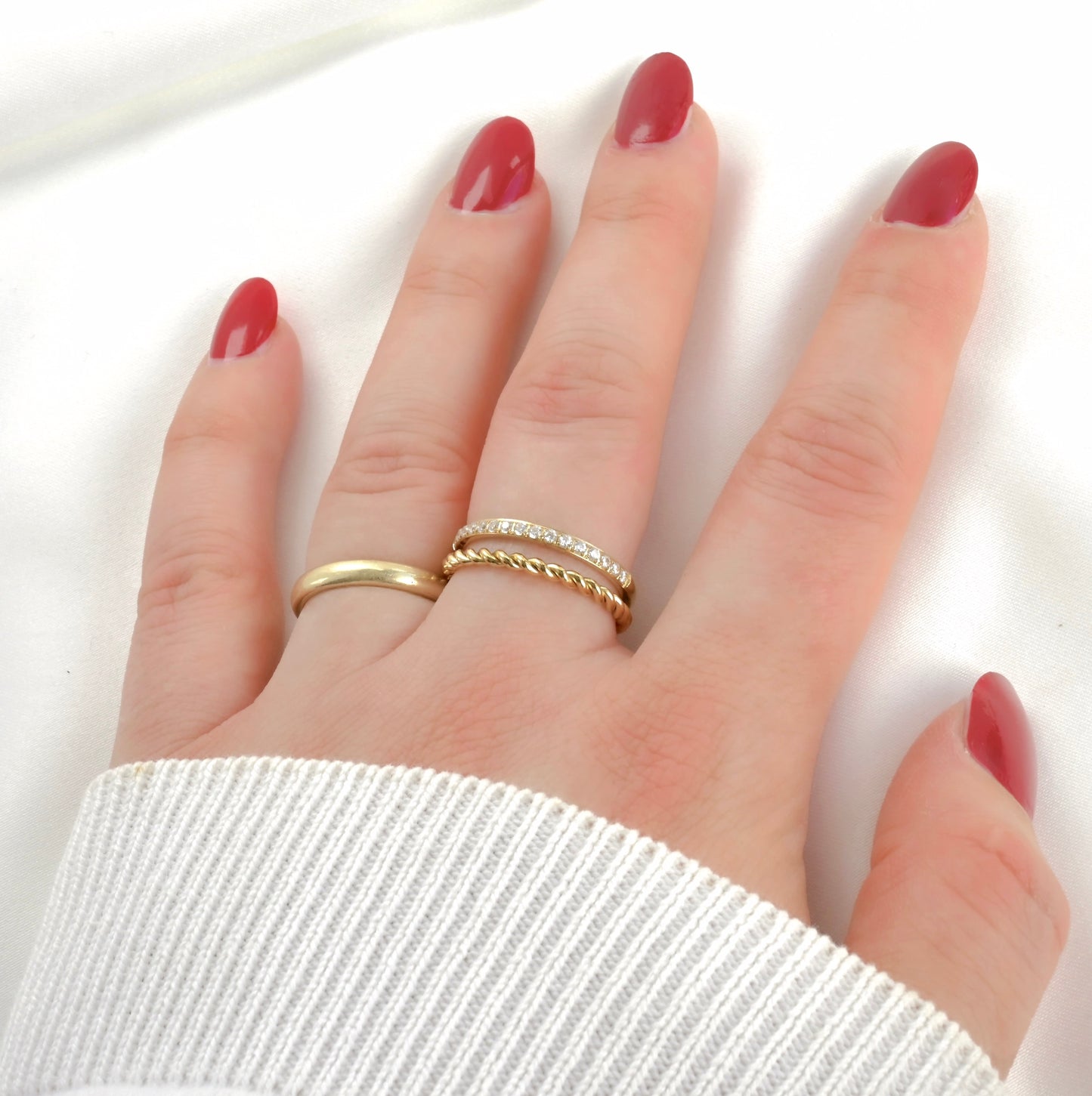Hand with red nail polish wearing layered gold ring with pave diamond accents on a white background