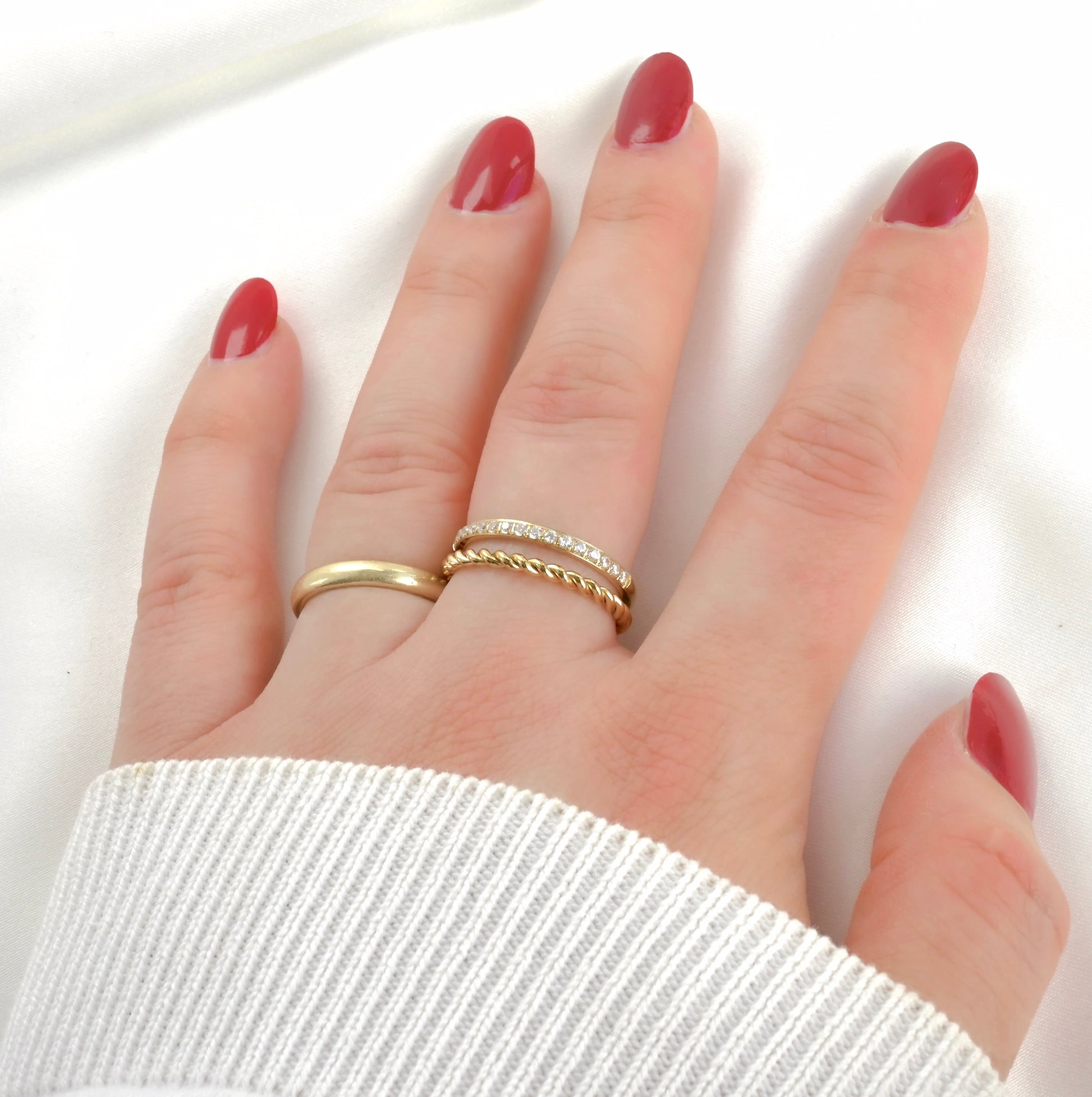 Hand with red nail polish wearing layered gold ring with pave diamond accents on a white background