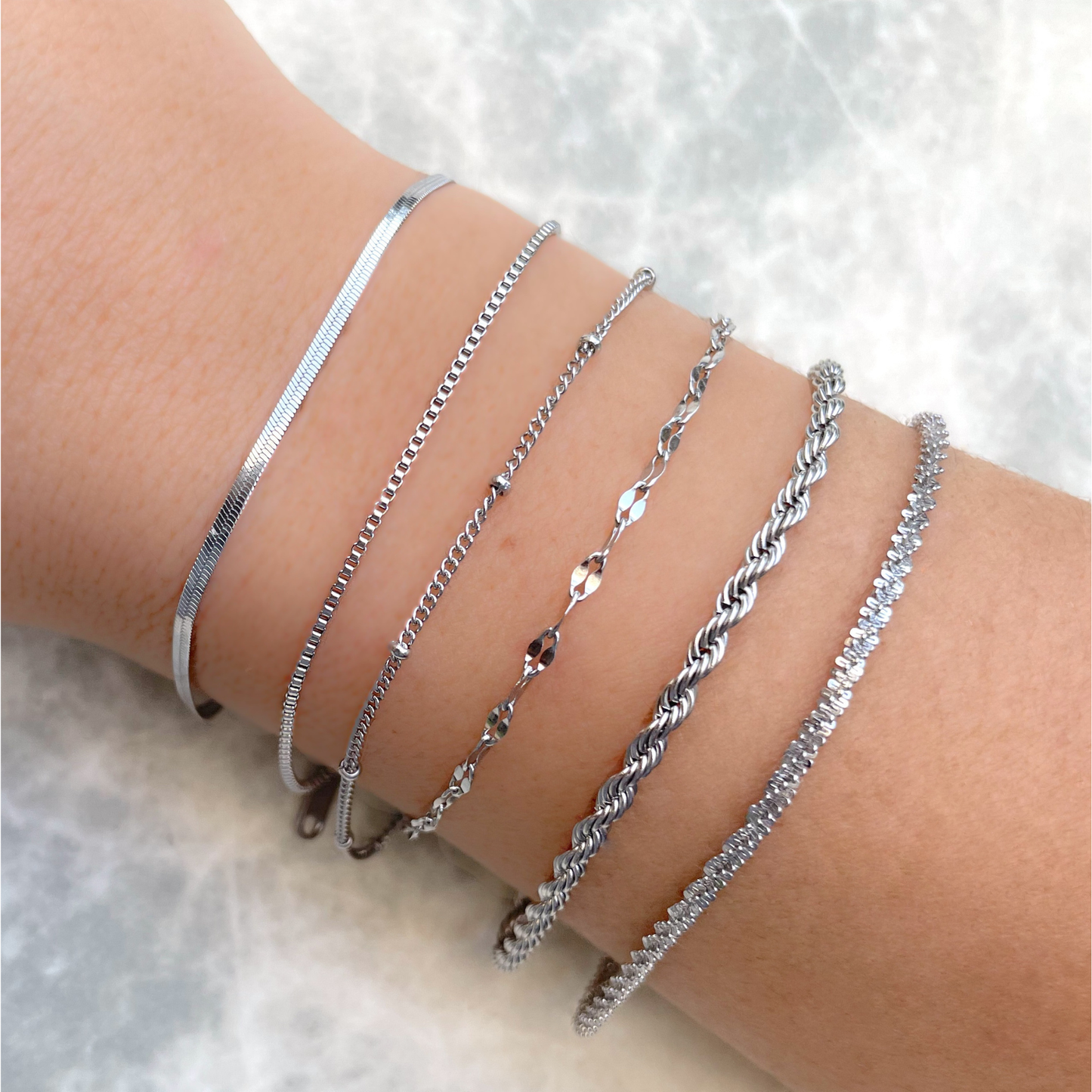 Dainty silver bracelets with high polish on a person's wrist against a light background