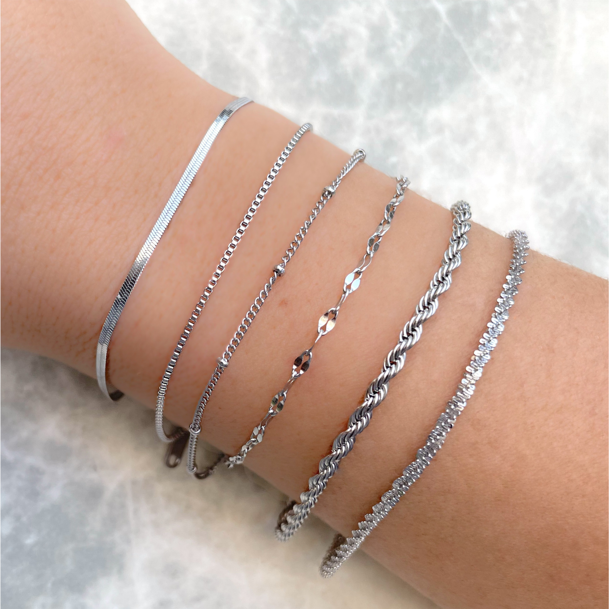 Dainty silver bracelets with high polish on a person's wrist against a light background