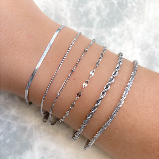 Dainty silver bracelets with high polish on a person's wrist against a light background