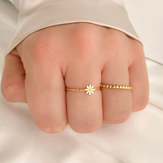 Gold ring with a daisy design on a person's finger against a neutral background