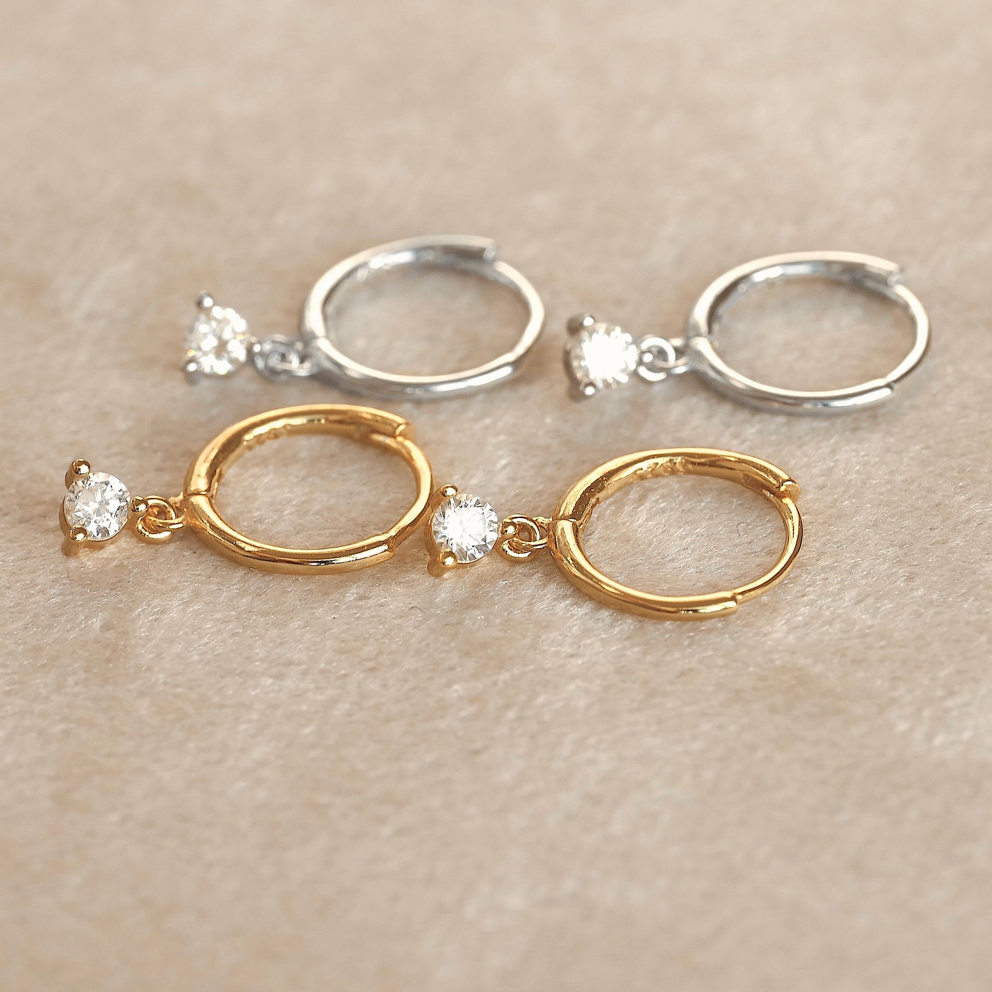 Pair of gold clicker hoop earrings with small diamond drops on a beige background