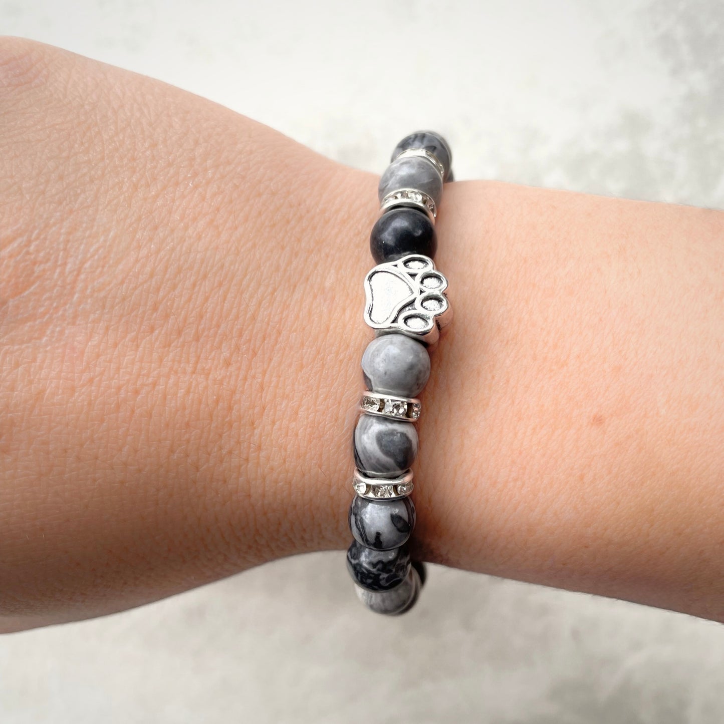 Bracelet with black and gray stones and a silver paw print charm on a wrist.