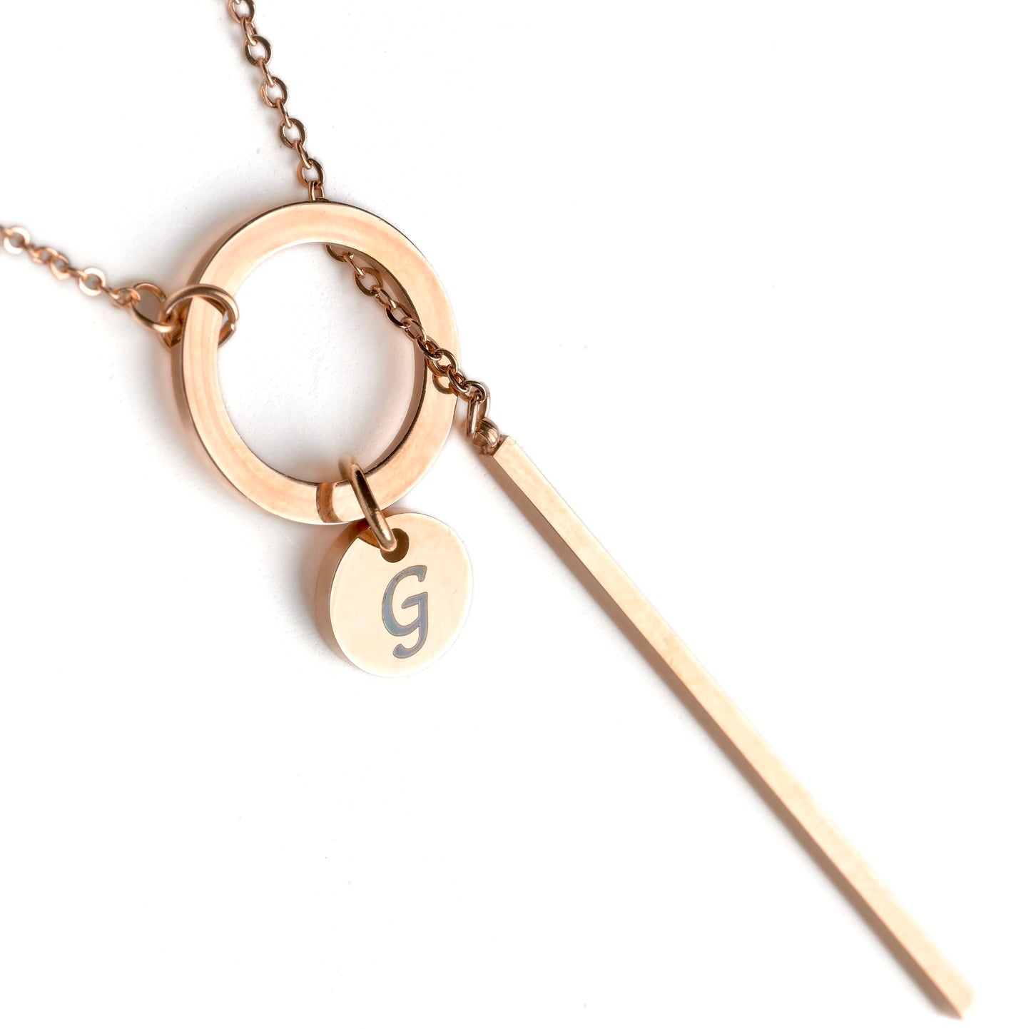 Rose gold necklace with a circular pendant and a small round tag with a letter 'G' on a white background.