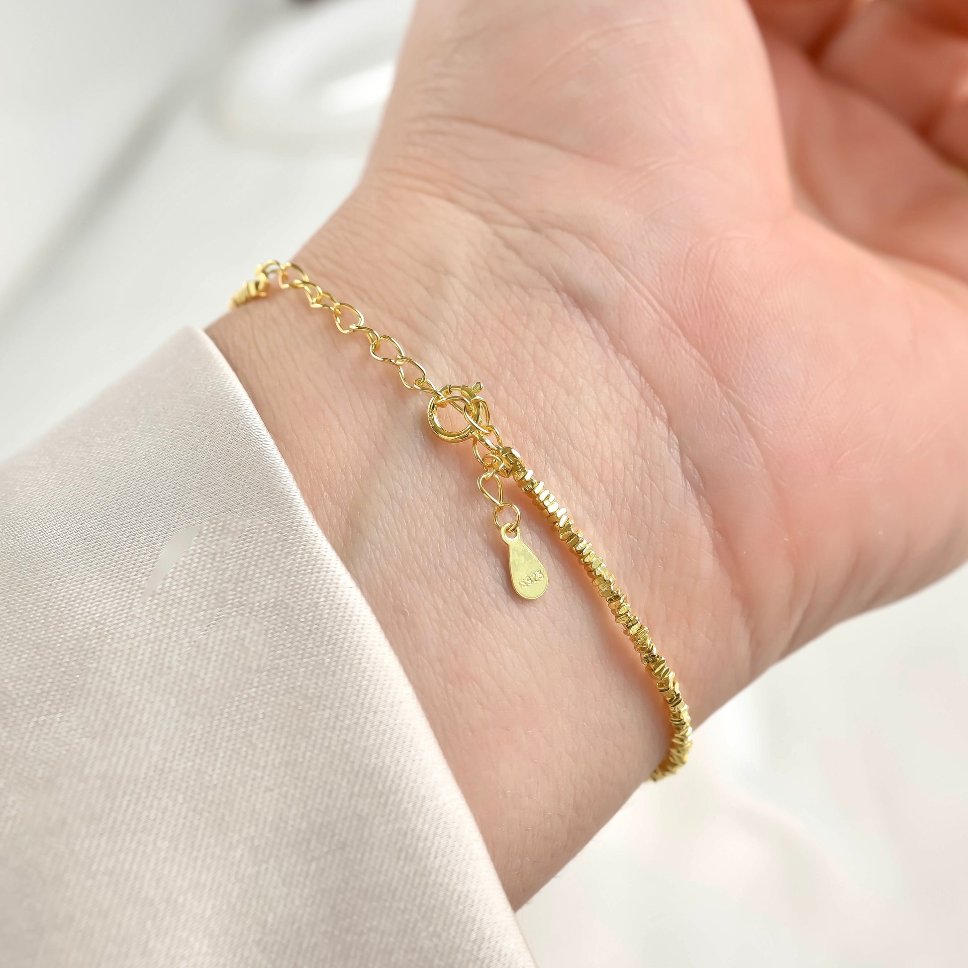 Gold beaded bracelet with an S925 tag on a wrist against a white background