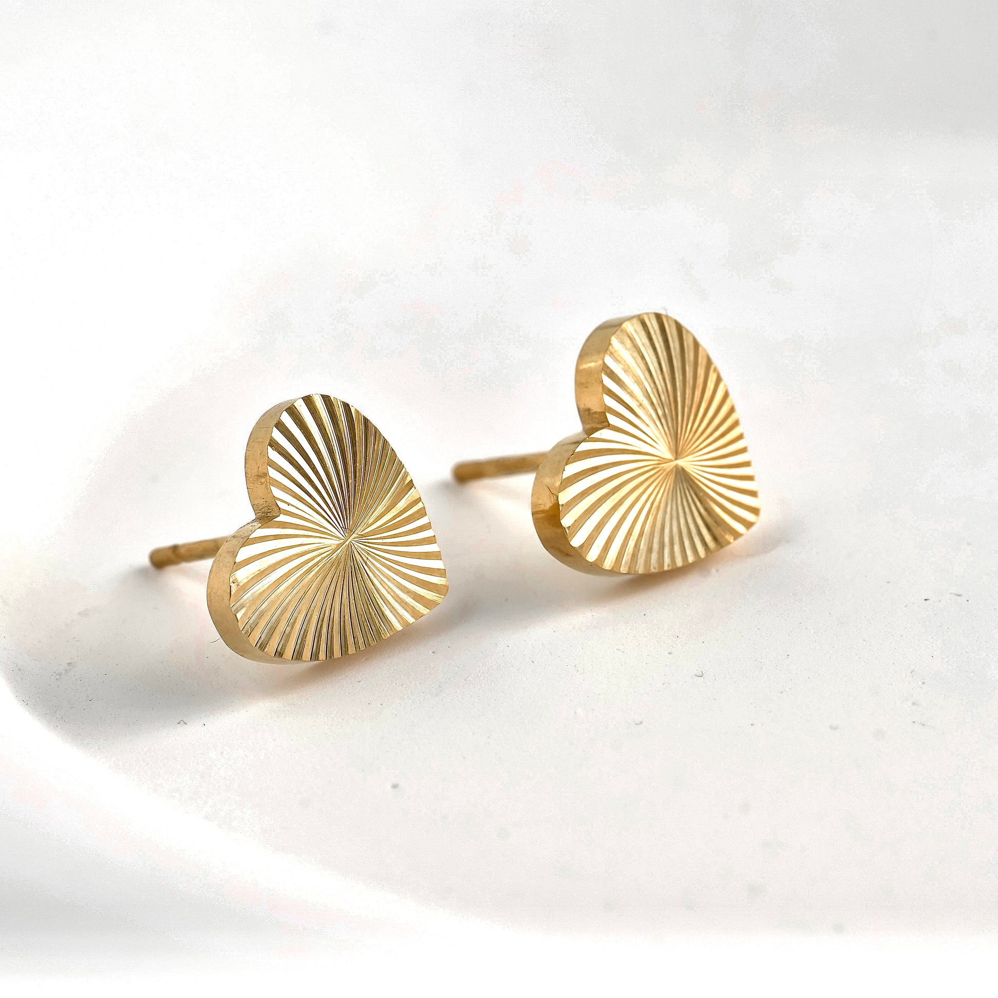 Pair of gold heart sunburst earrings on a white background