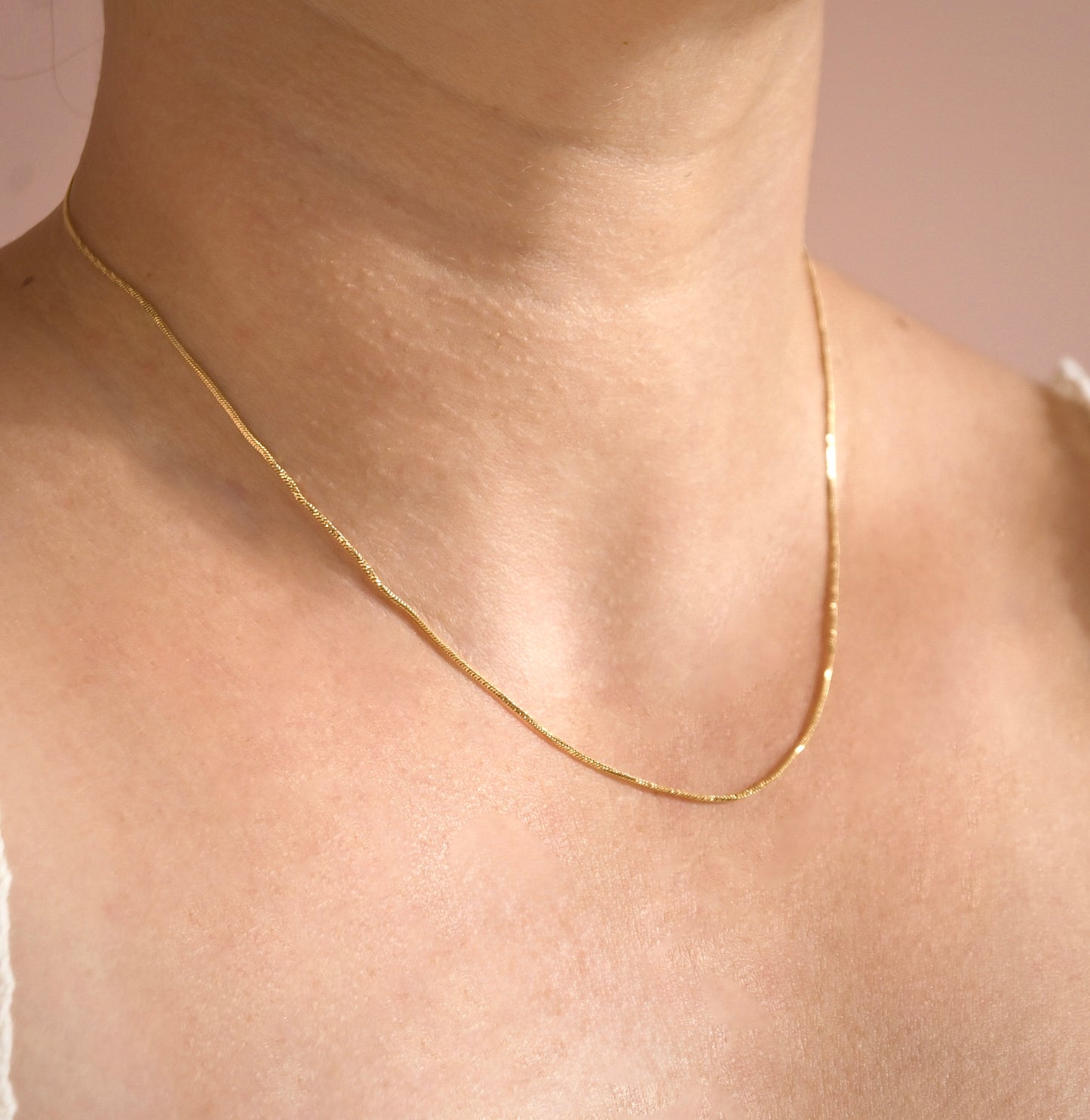 Gold snake chain necklace with shimmering twists on a person's neck with a neutral background