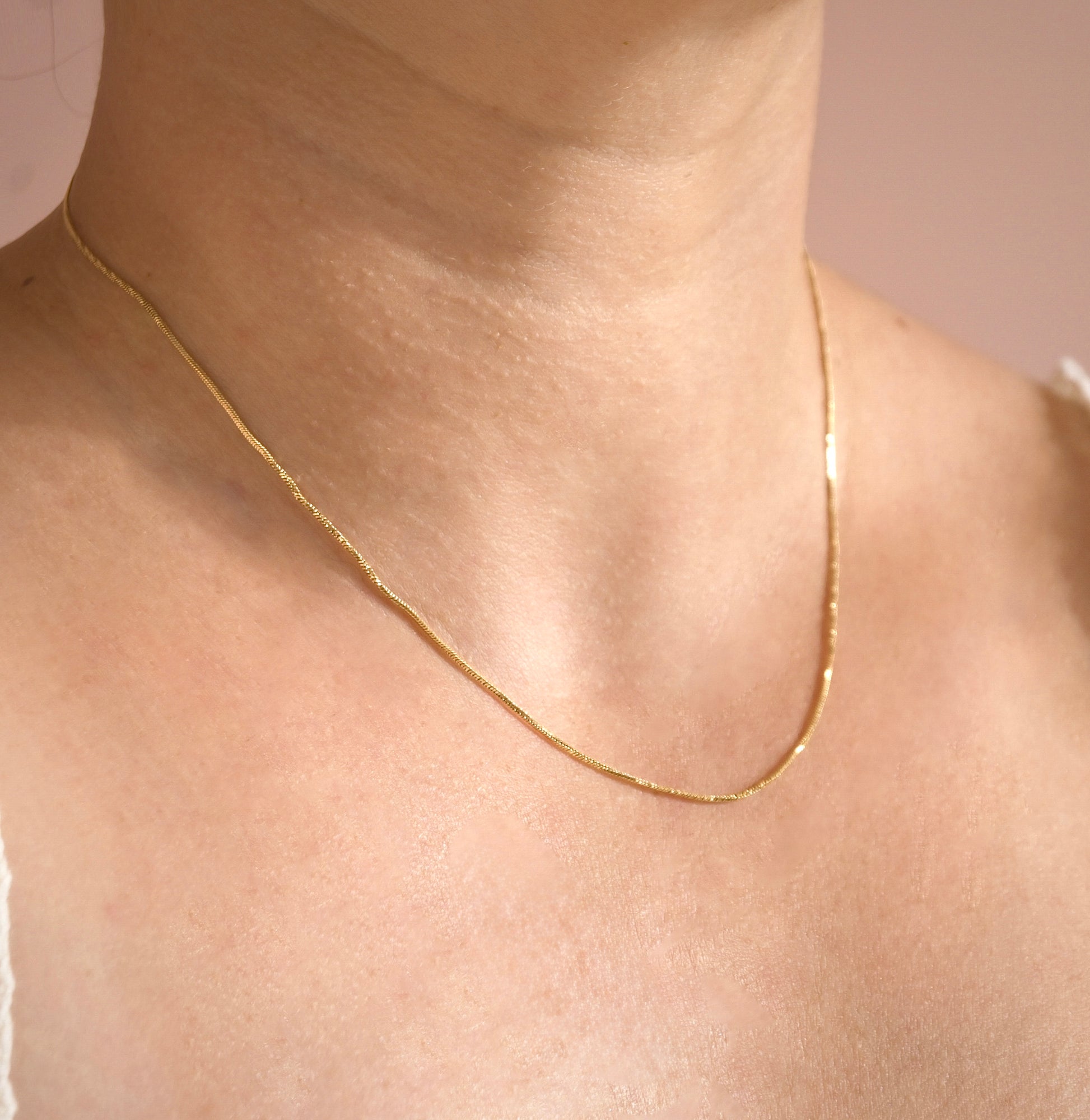 Gold snake chain necklace with shimmering twists on a person's neck with a neutral background