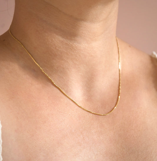 Gold snake chain necklace with shimmering twists on a person's neck with a neutral background