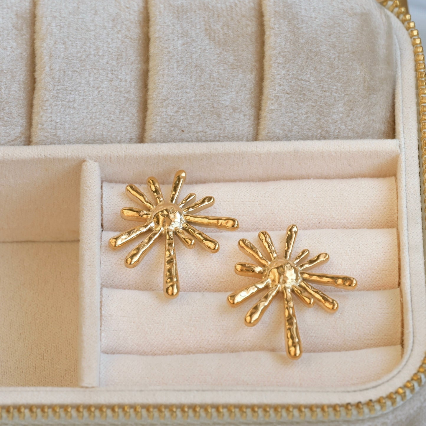Gold earrings on a beige jewelry case