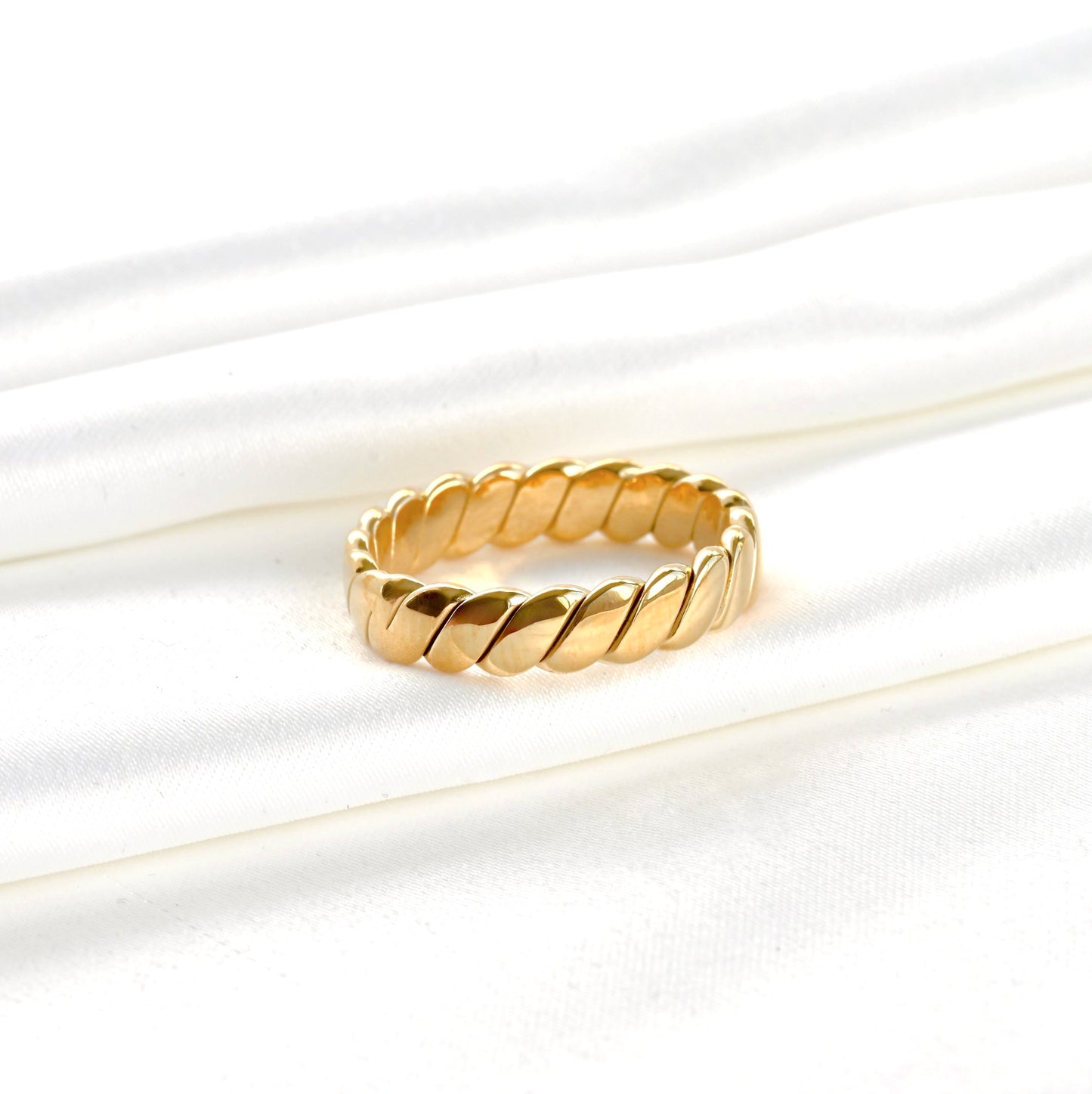 Wide gold ring with a braided design on a white background
