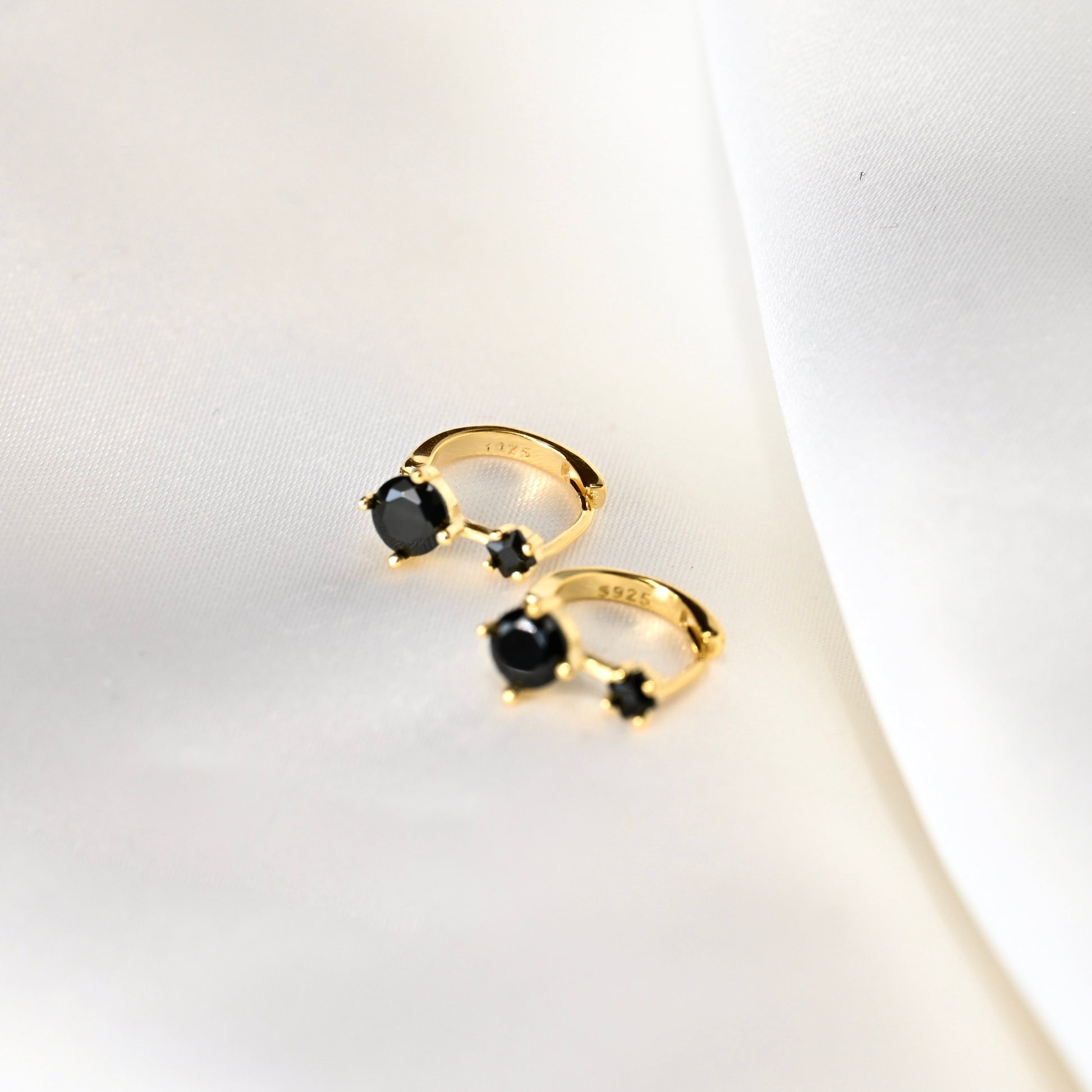 Gold hoop earrings with two black gemstones on a white background