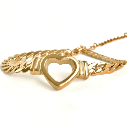 Chunky gold racelet with a heart charm on a white background