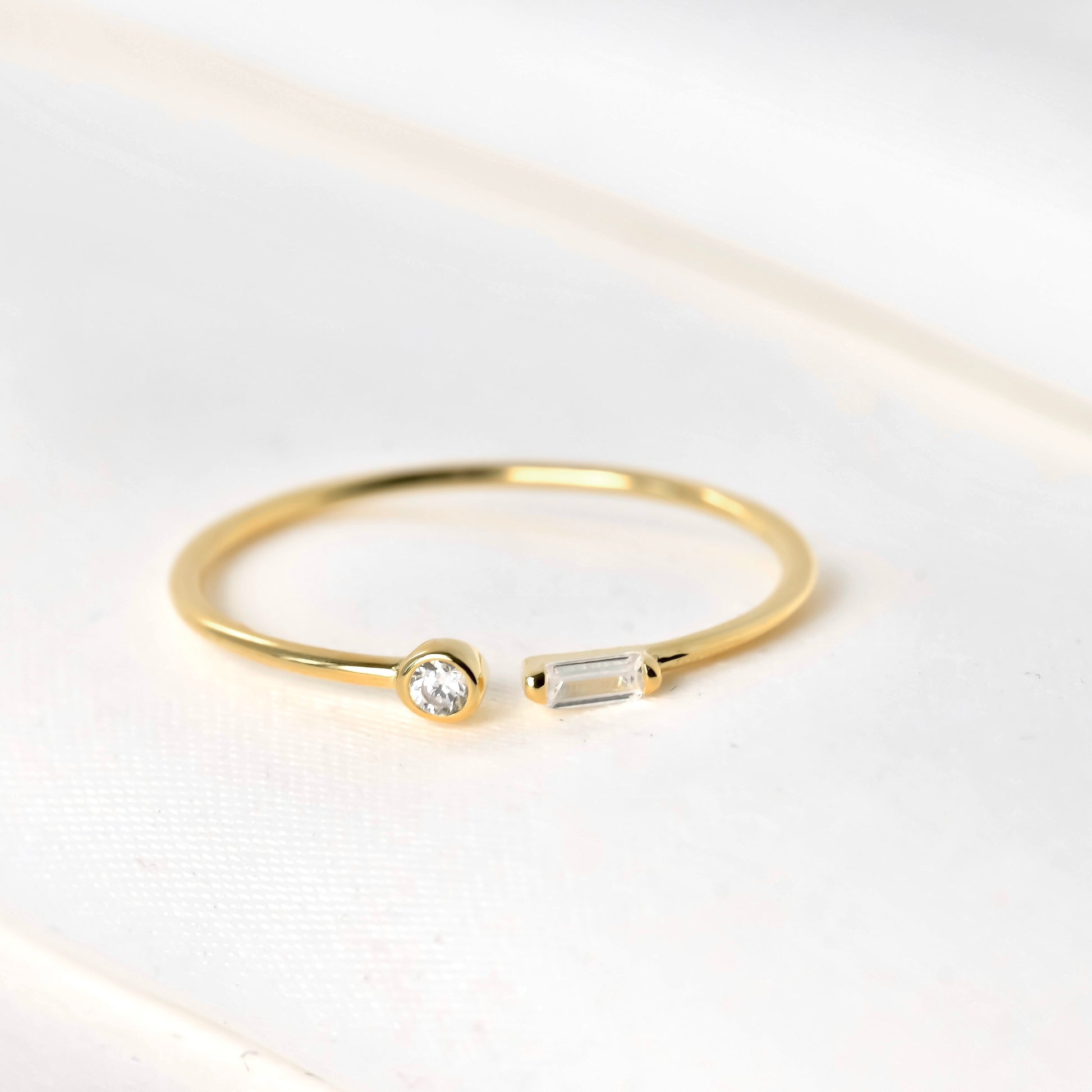 Gold open ring with two diamonds, one baguette and one bezel on a light background
