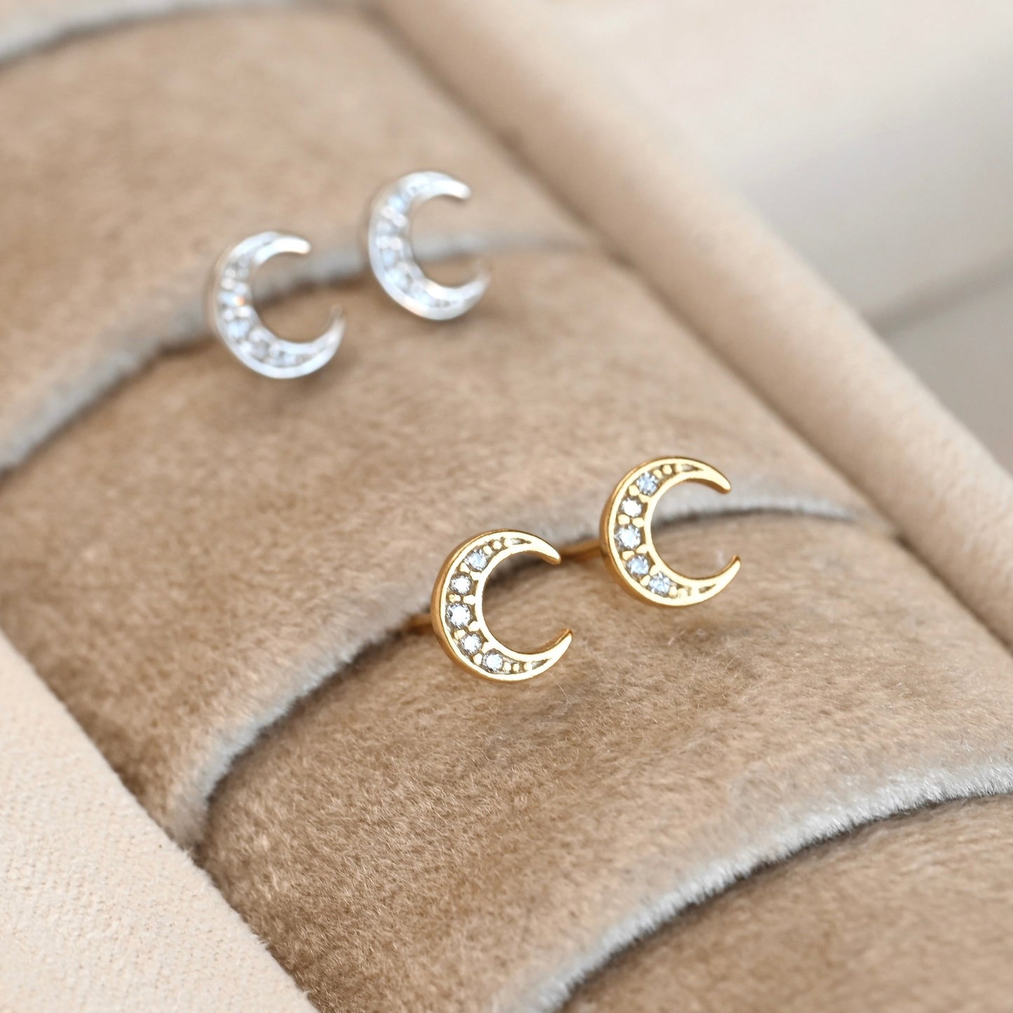Gold and silver moon-shaped earrings on a beige fabric background