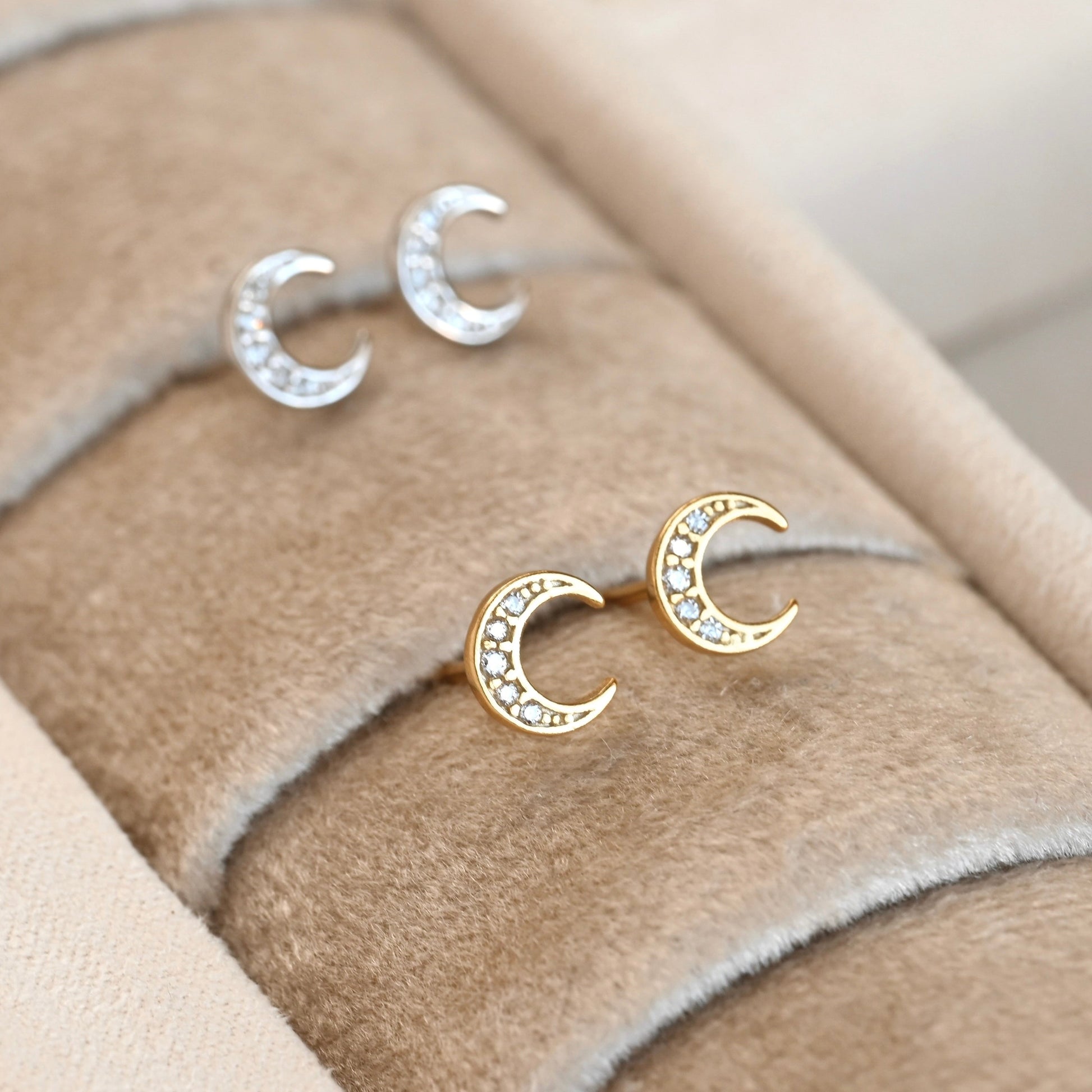 Gold and silver moon-shaped earrings on a beige fabric background