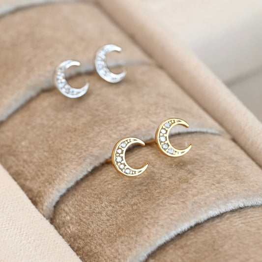 Gold and silver moon-shaped earrings on a beige fabric background