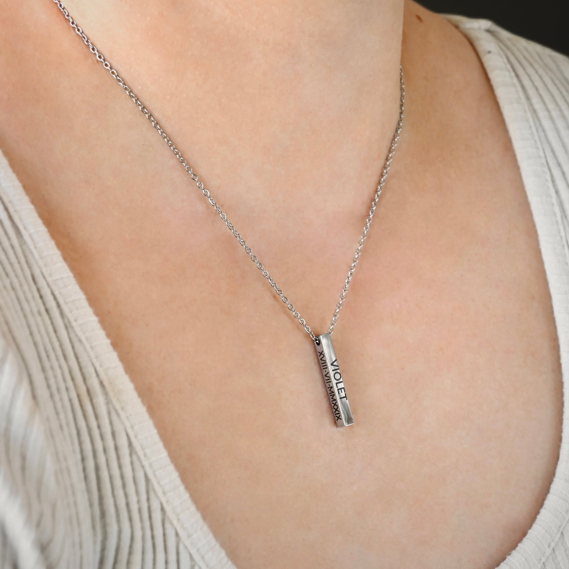 Silver necklace with an engraved bar pendant on a person wearing a beige top.
