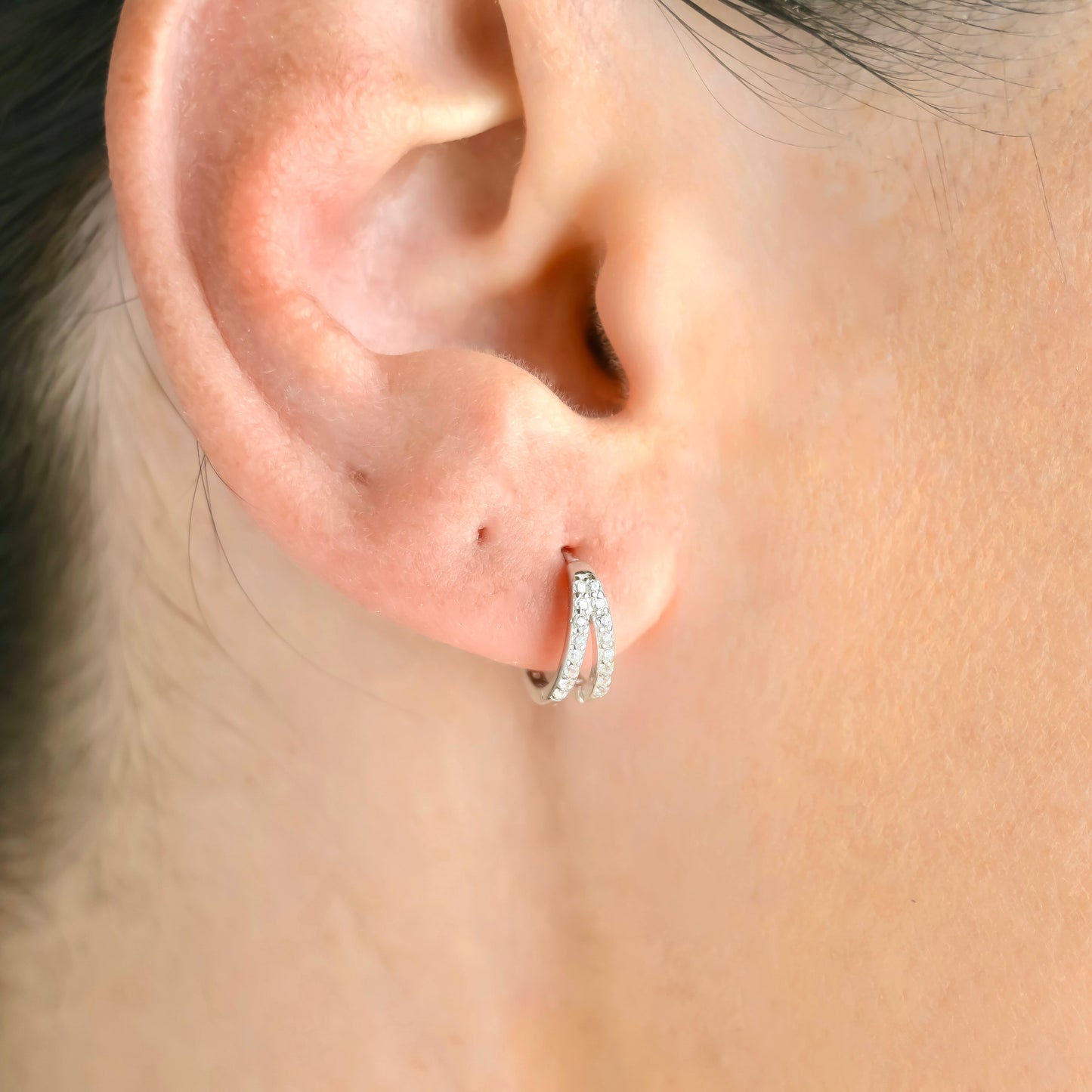 Close-up of an ear wearing a silver layered pave CZ hoop earring with a blurred background