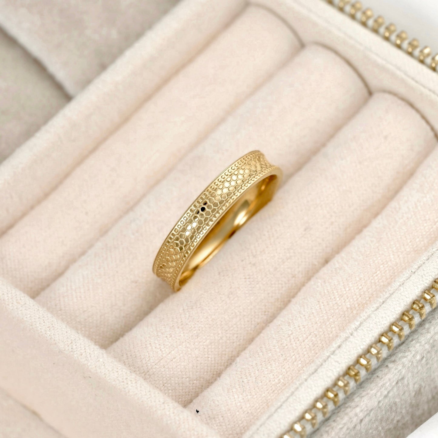 A gold ring with an intricate textured snake skin pattern, displayed inside a cream-colored velvet jewelry box.