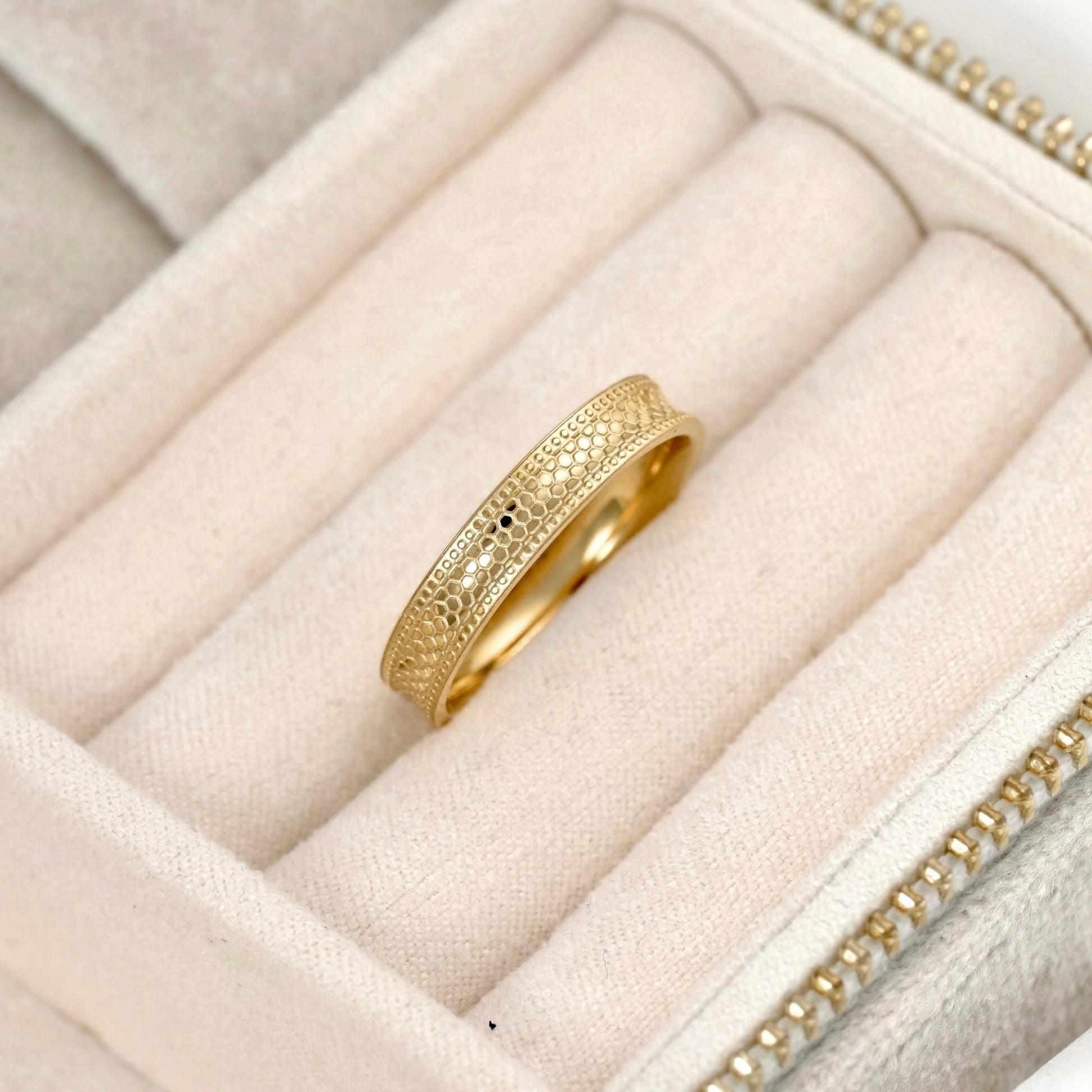 A gold ring with an intricate textured snake skin pattern, displayed inside a cream-colored velvet jewelry box.