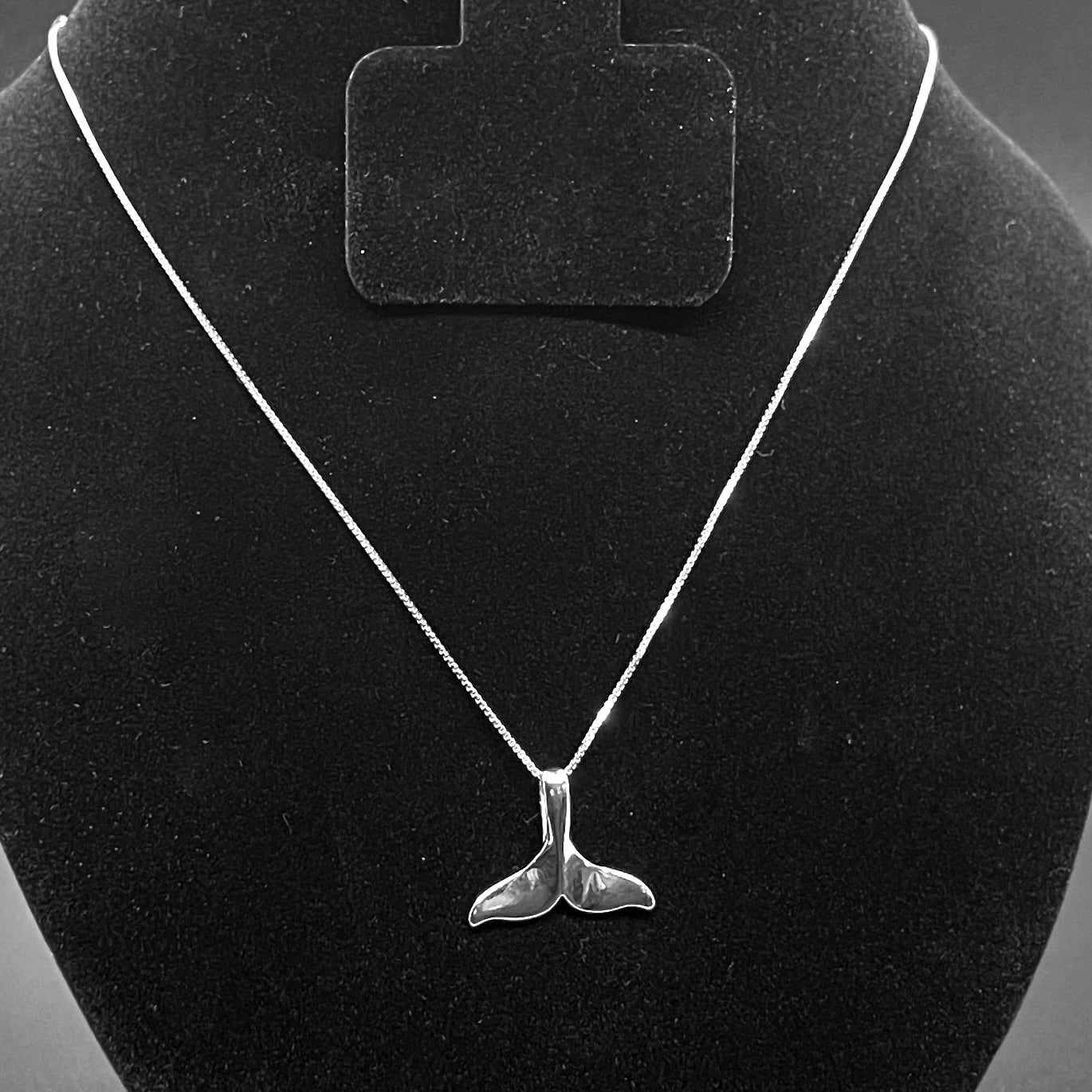 Silver whale tail necklace on a black velvet stand