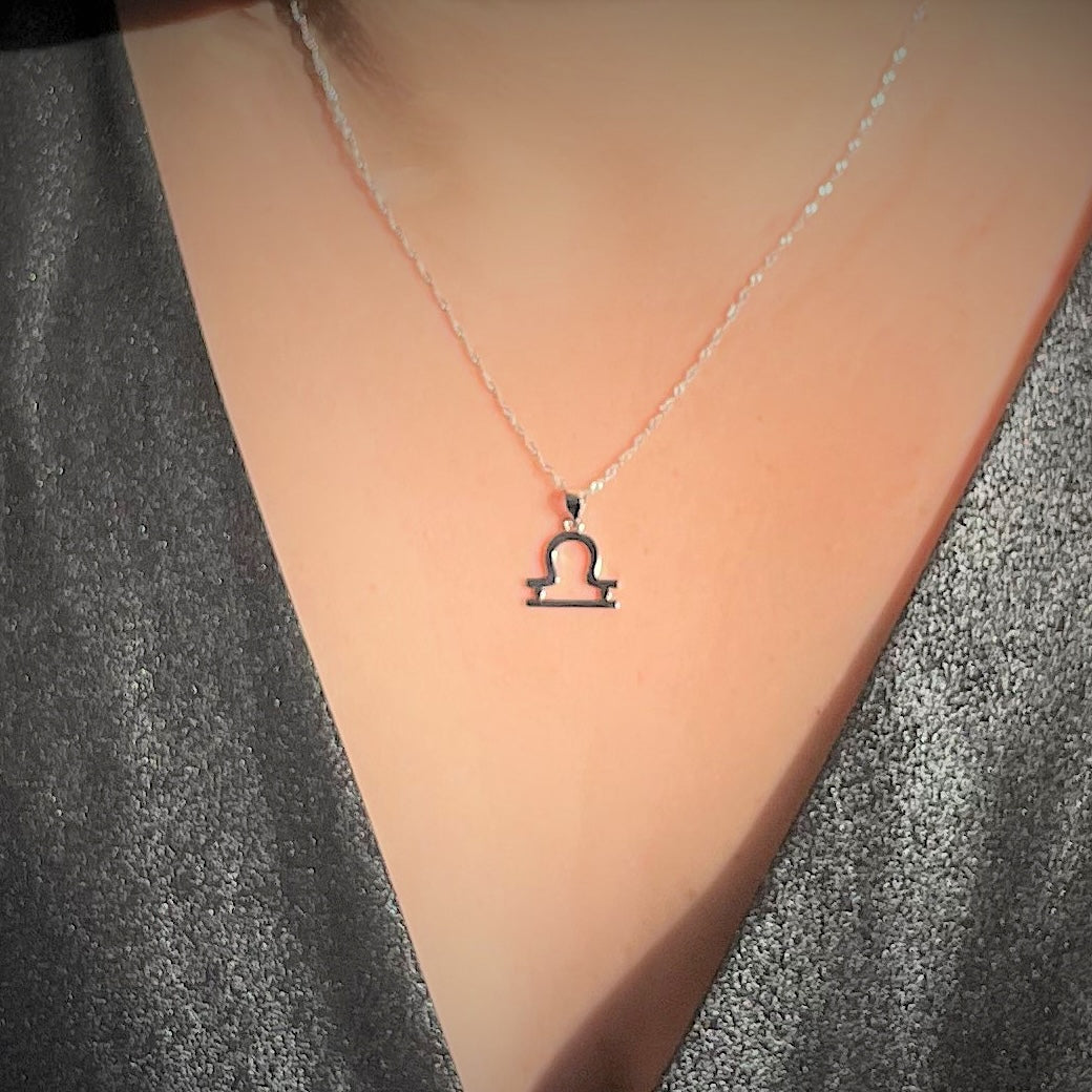 Silver necklace with a Libra zodiac pendant on a person wearing a gray top.