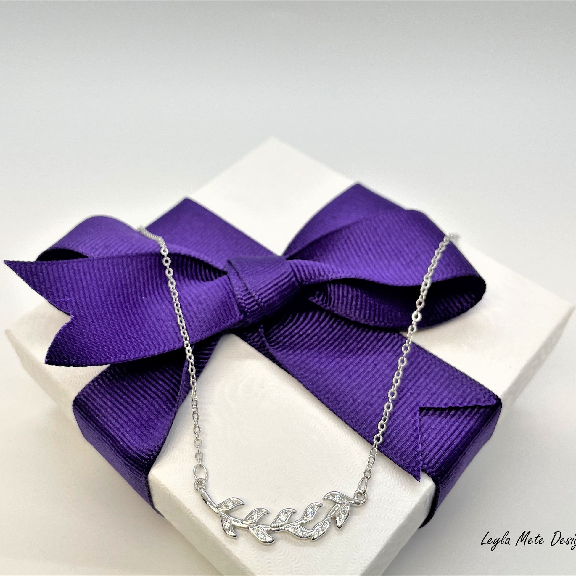 Silver necklace on a white box with a purple ribbon, branded 'Leyla Mete Design Studio'.