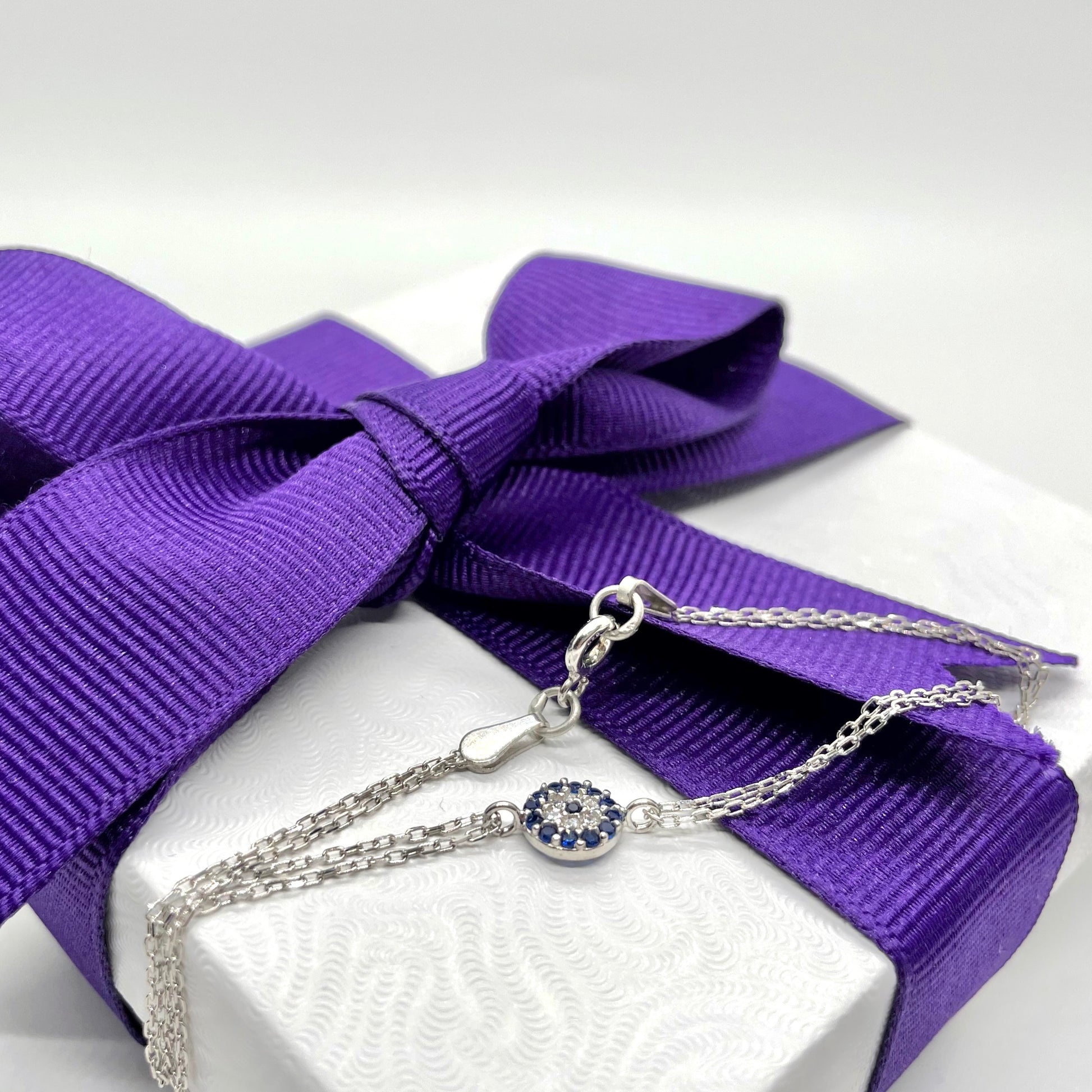 Silver bracelet with a blue eye connector on a white box with a purple ribbon