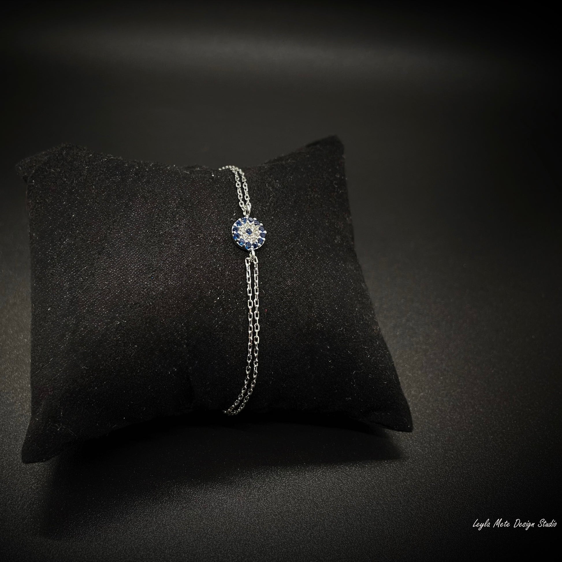 Silver nazar bracelet with a blue gemstone on a black cushion against a dark background