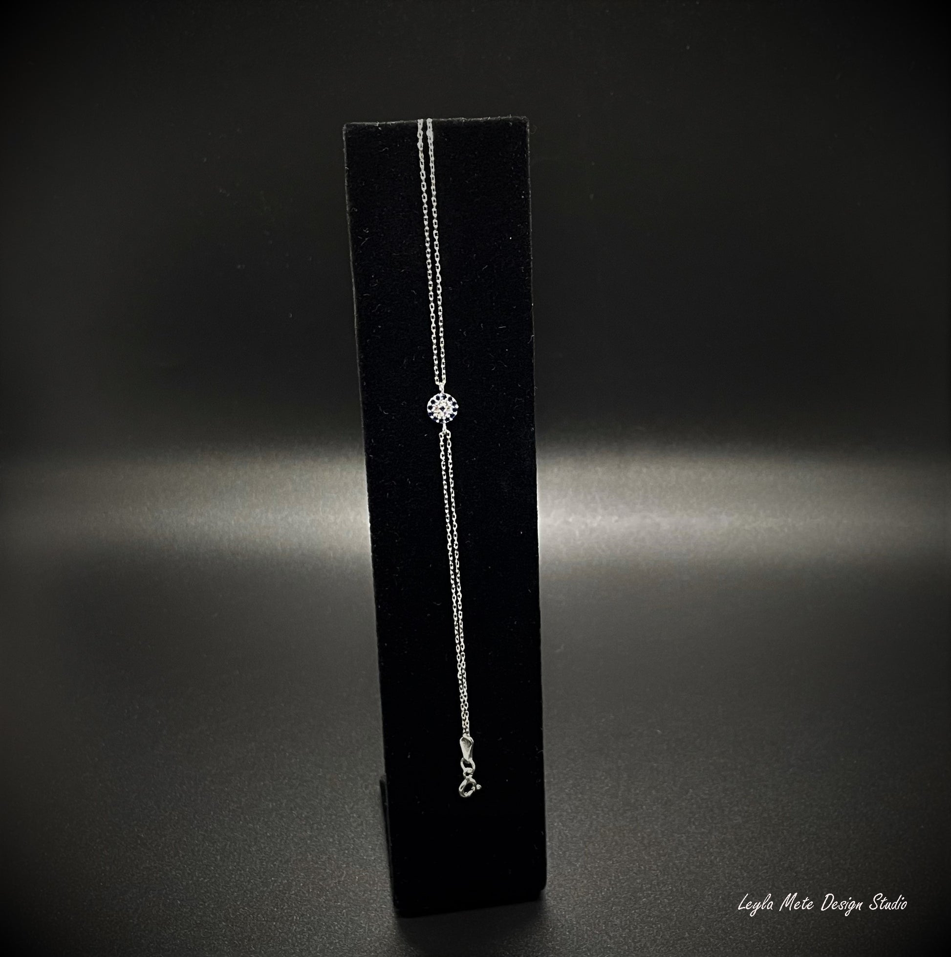 Silver evil eye bracelet with a spring ring clasp on a black bracelet stand against a dark background