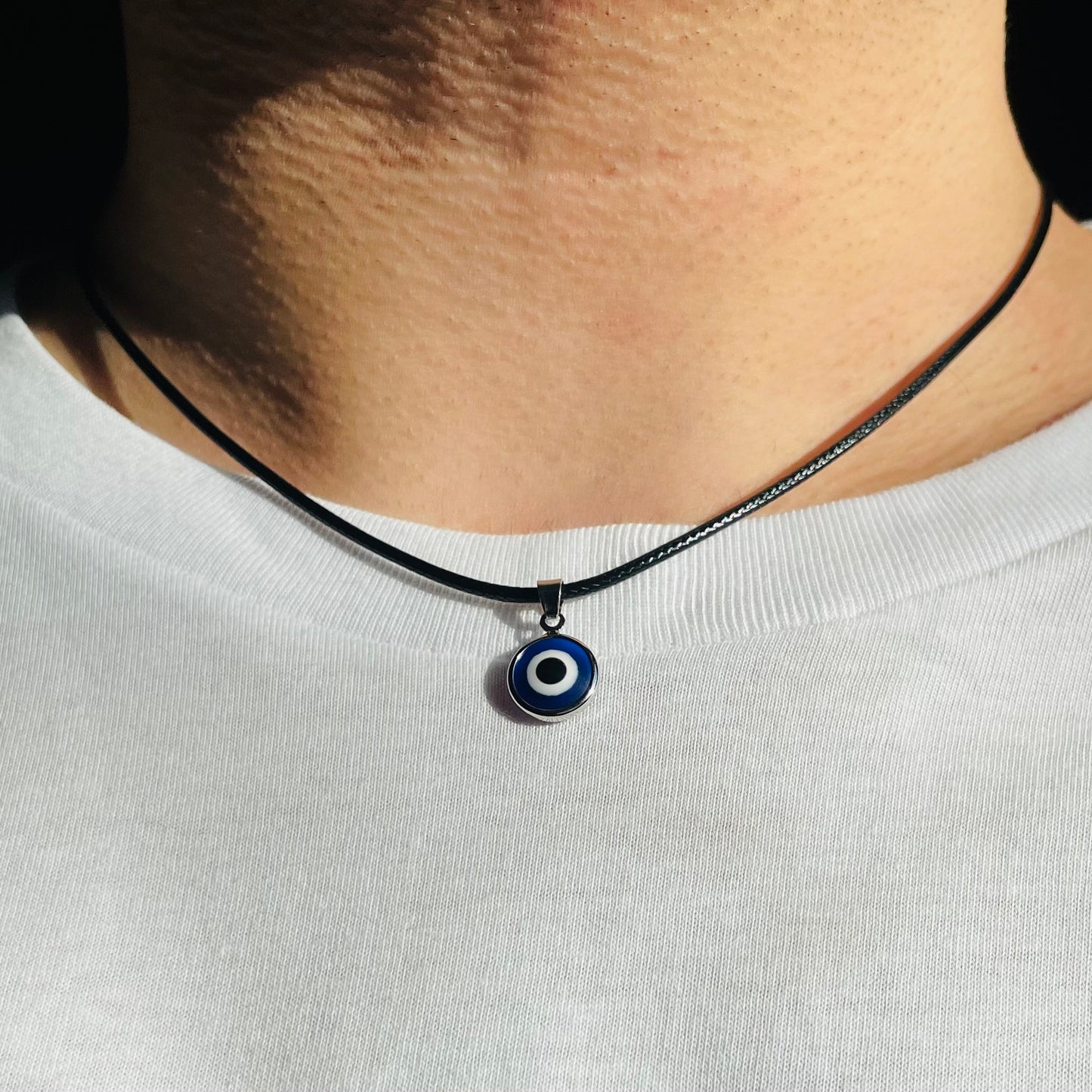 Necklace with small round eye charm worn by a man on a white shirt.