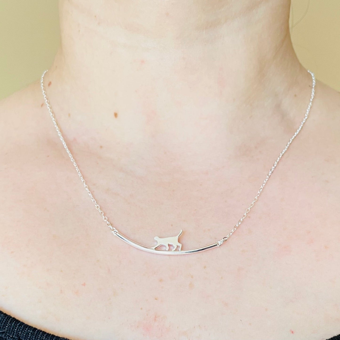 Front view of 18-inch silver necklace with a curved bar and cat silhouette on it, on a person's neck against a neutral background