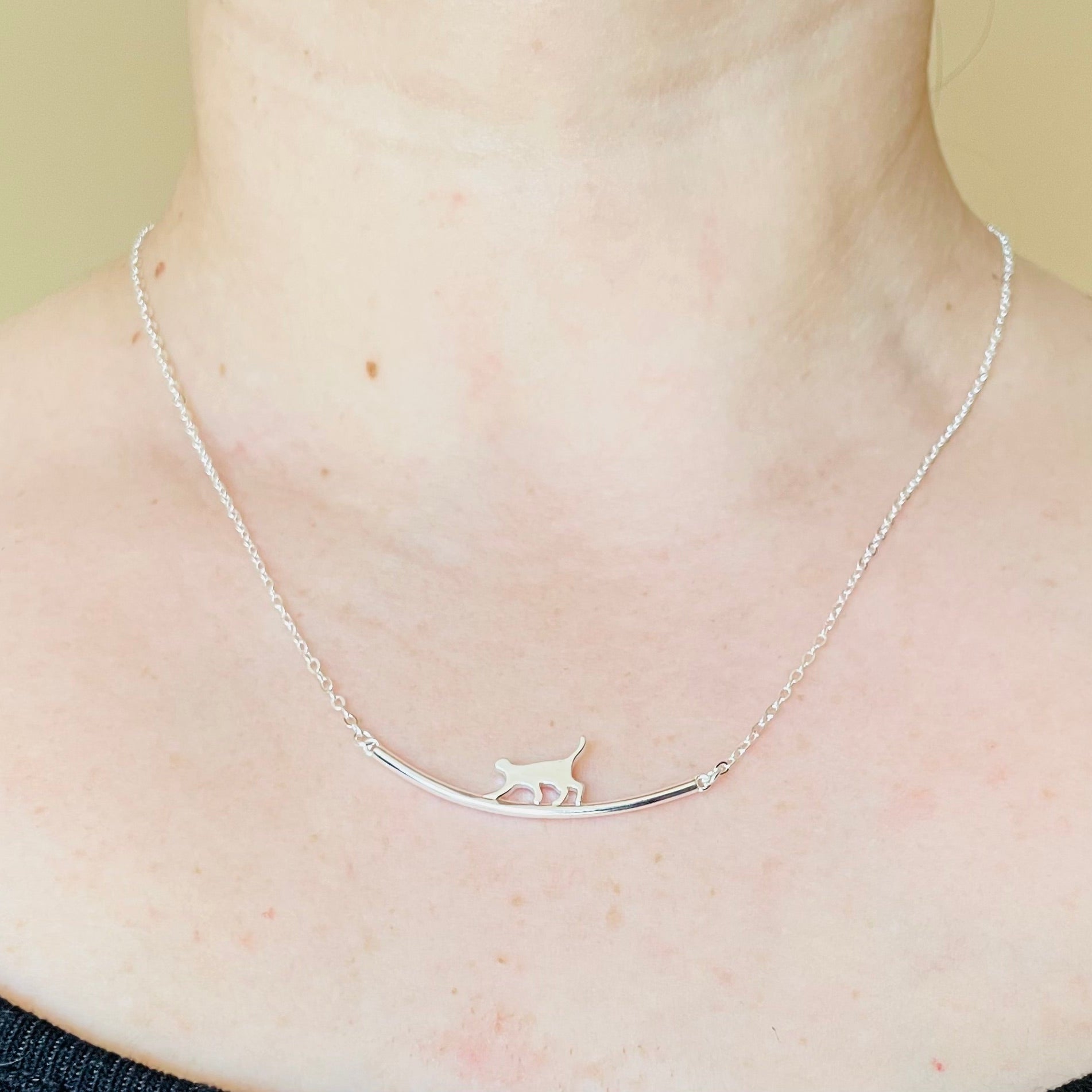 Front view of 18-inch silver necklace with a curved bar and cat silhouette on it, on a person's neck against a neutral background