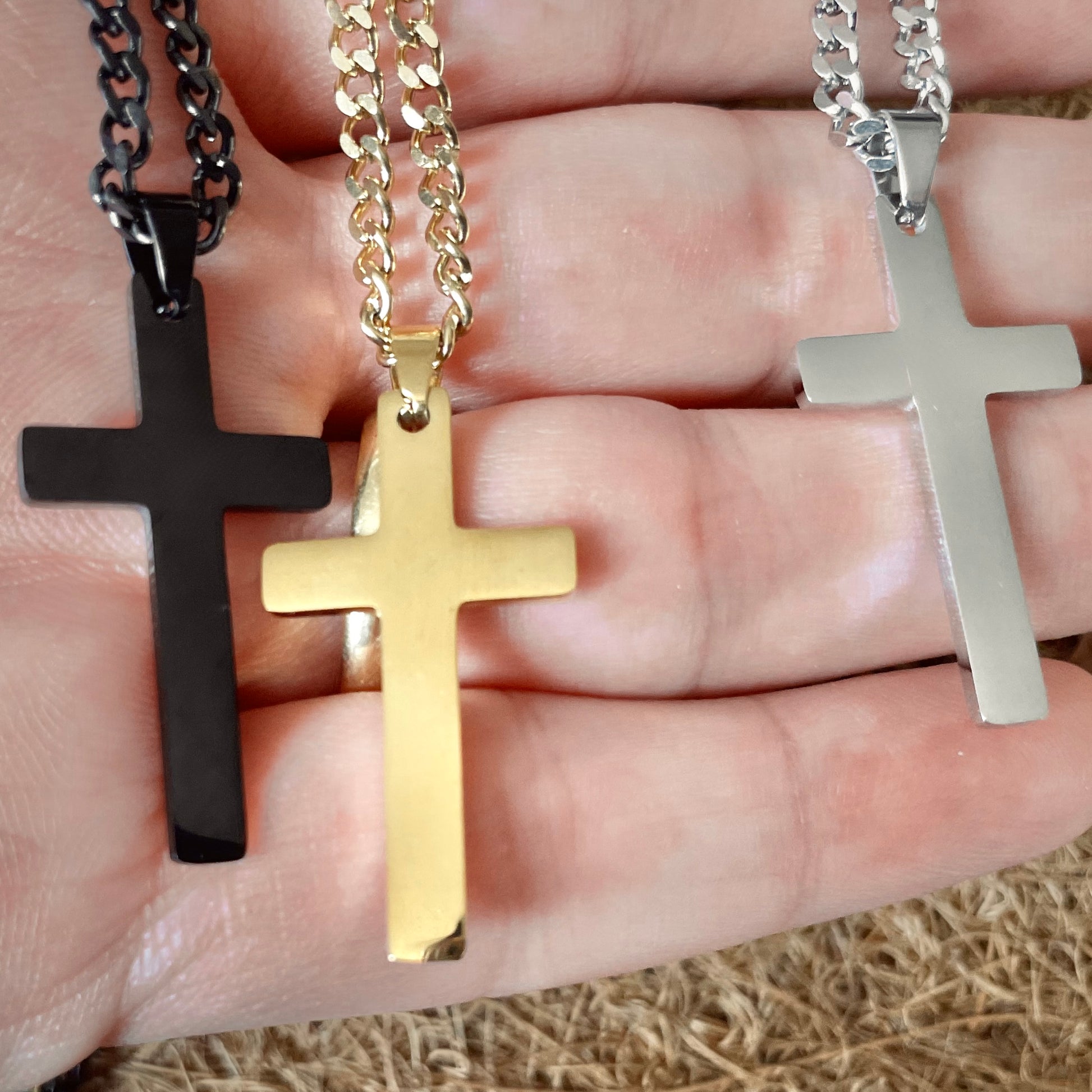 Three cross-shaped pendants in black, gold, and silver held in a hand.