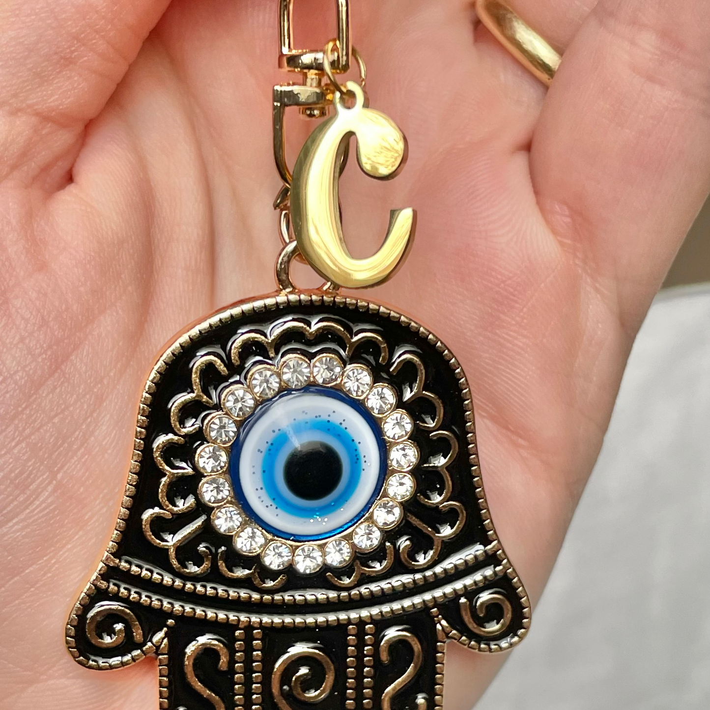 Decorative hamsa keychain with eye design and 'C' initial held in a hand