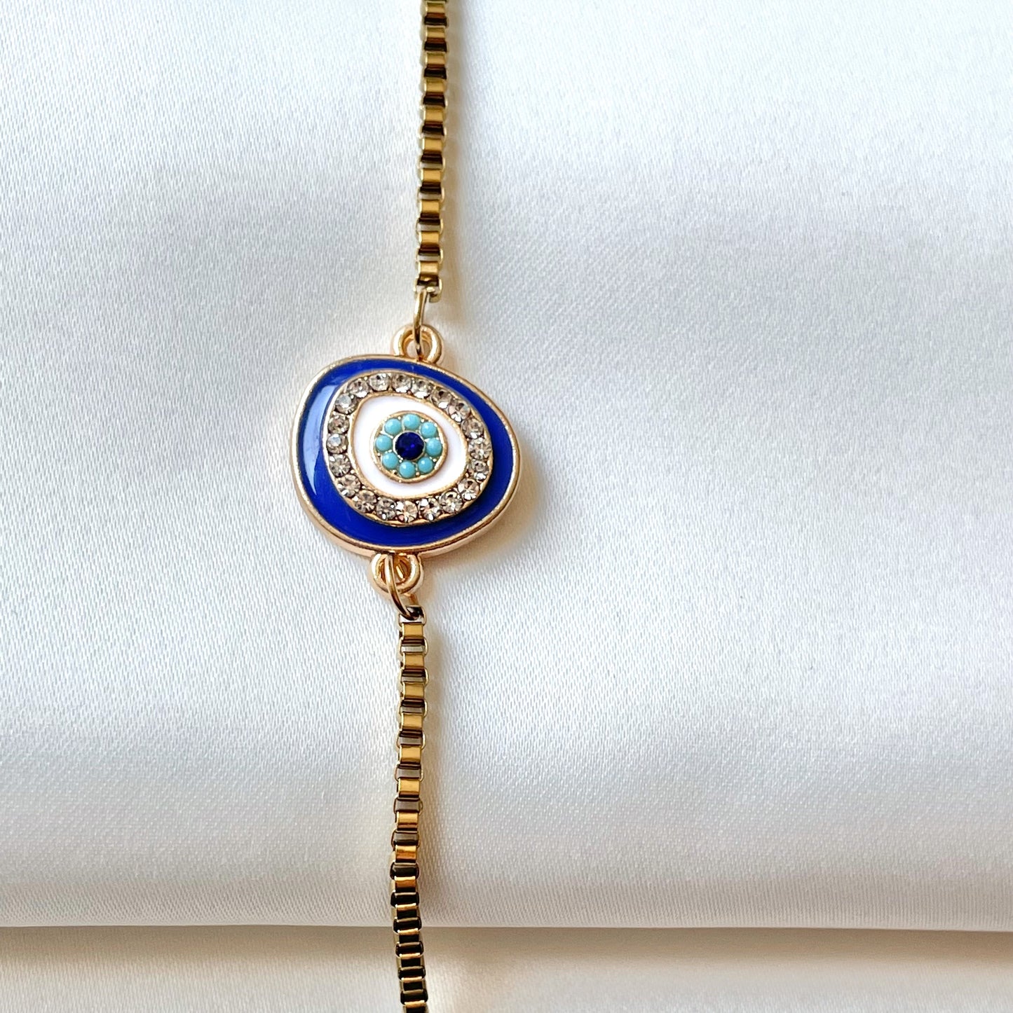 Gold anklet with a blue evil eye pendant vertically positioned on a white background