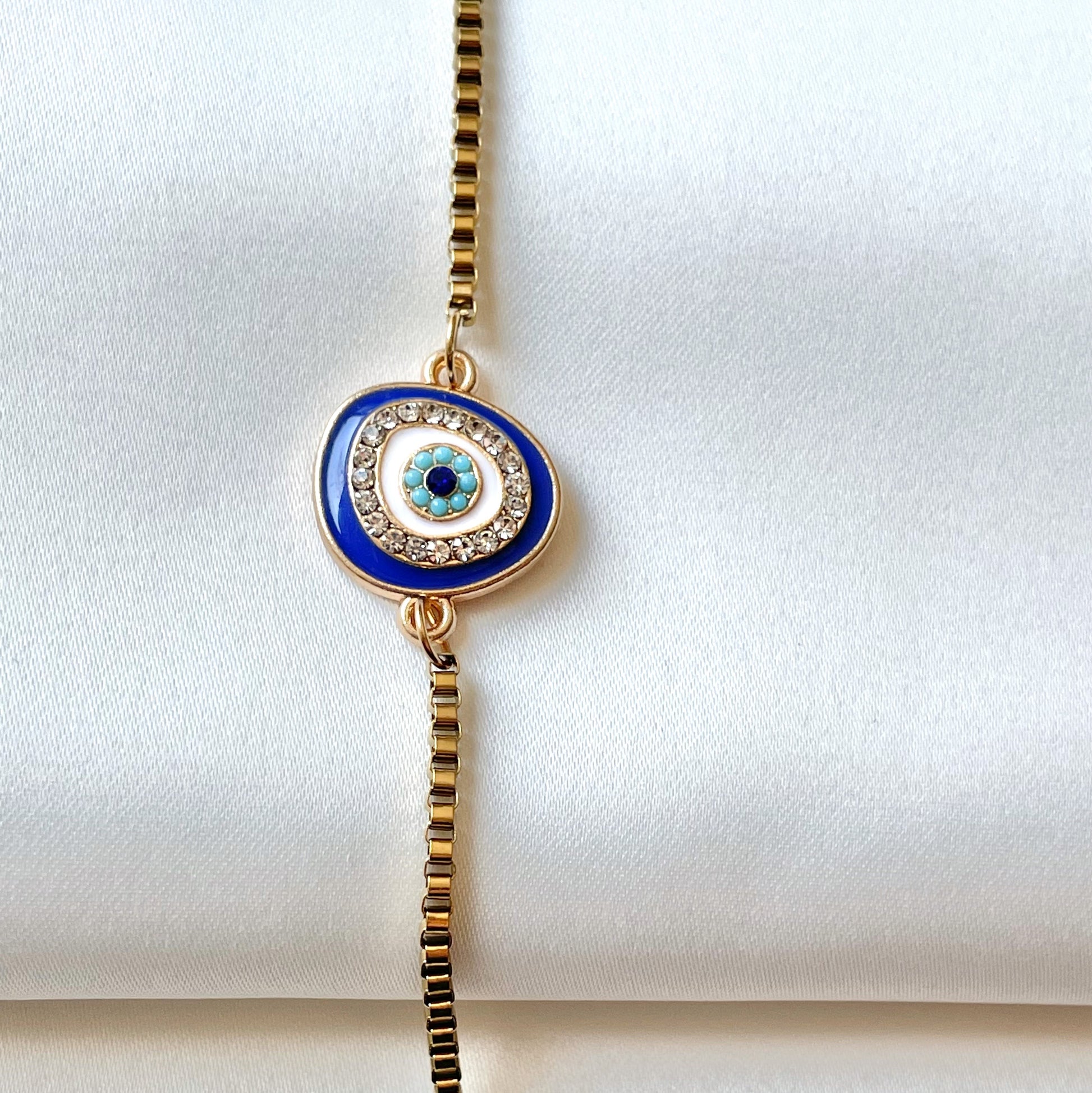 Gold anklet with a blue evil eye pendant vertically positioned on a white background
