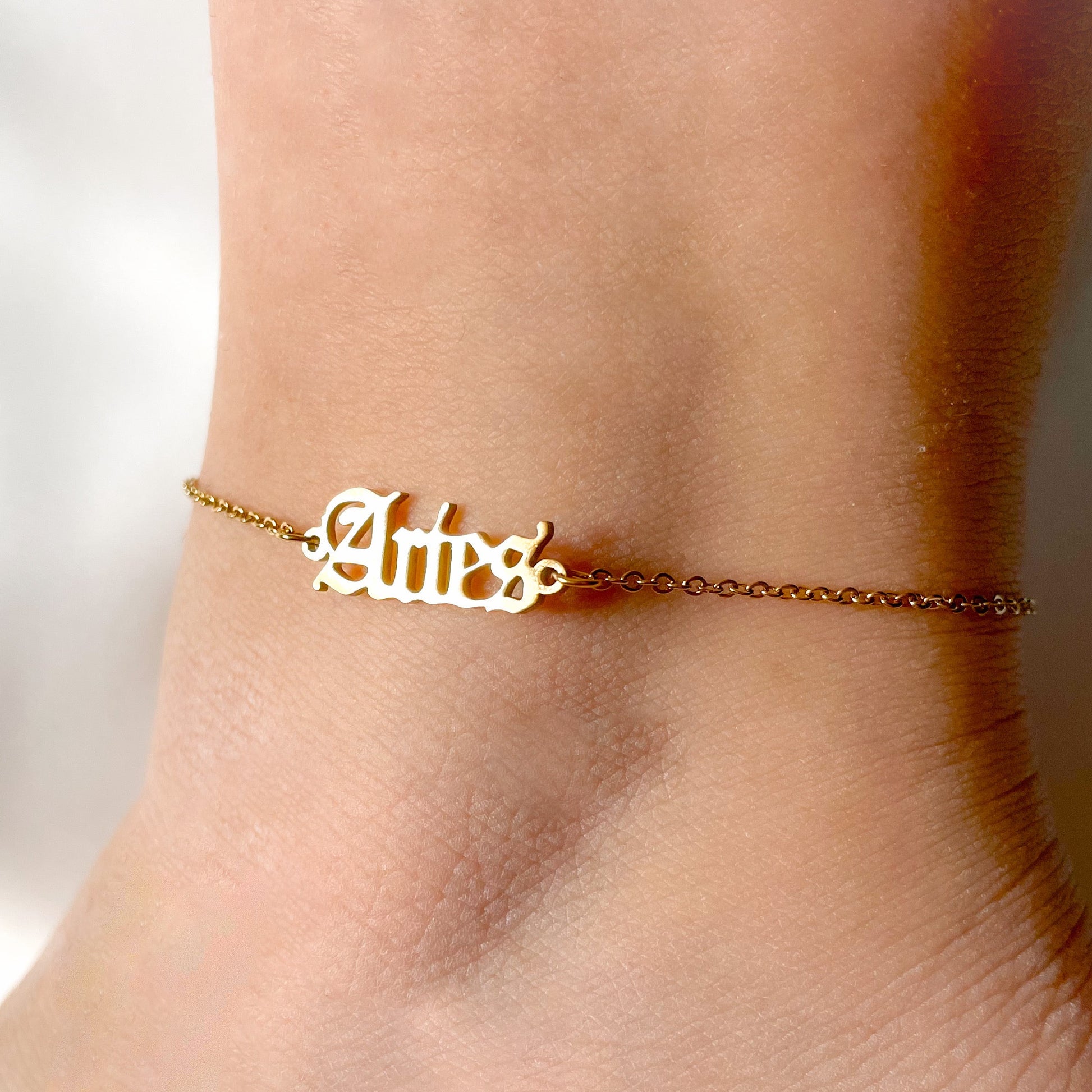 Gold anklet with 'Aries' on a person's ankle against a blurred background