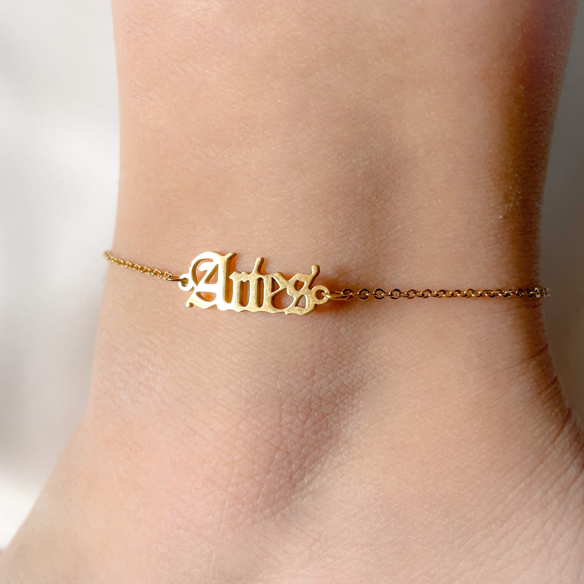 Gold 'Aries' ankle bracelet on an ankle with a blurred background