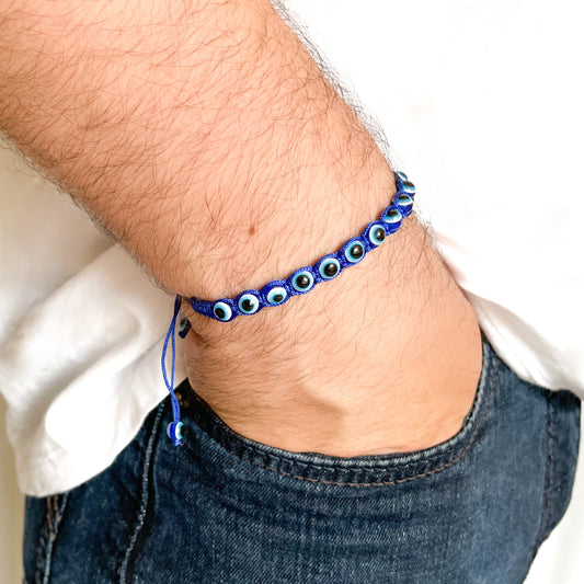 Blue evil eye bracelet with beads on a man's wrist against a neutral background