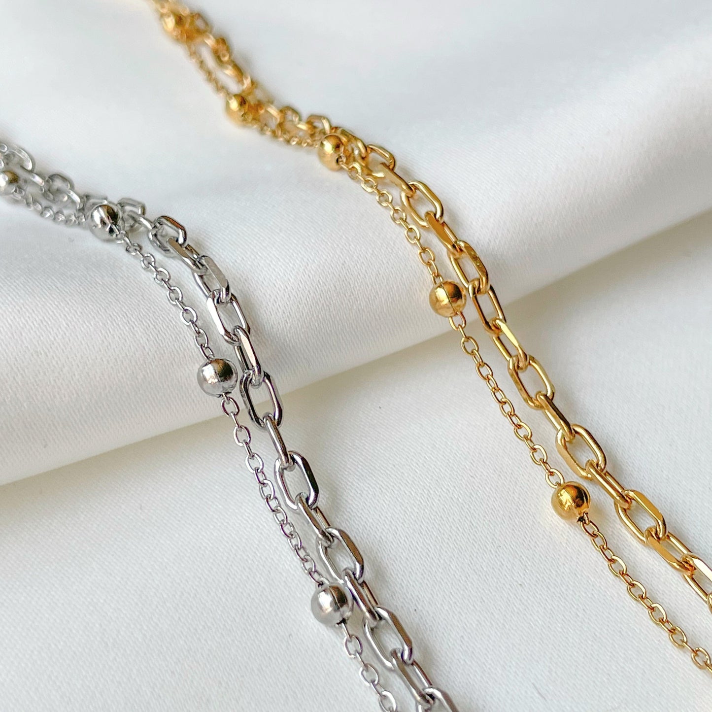 Two gold and silver chain bracelets on a white fabric background