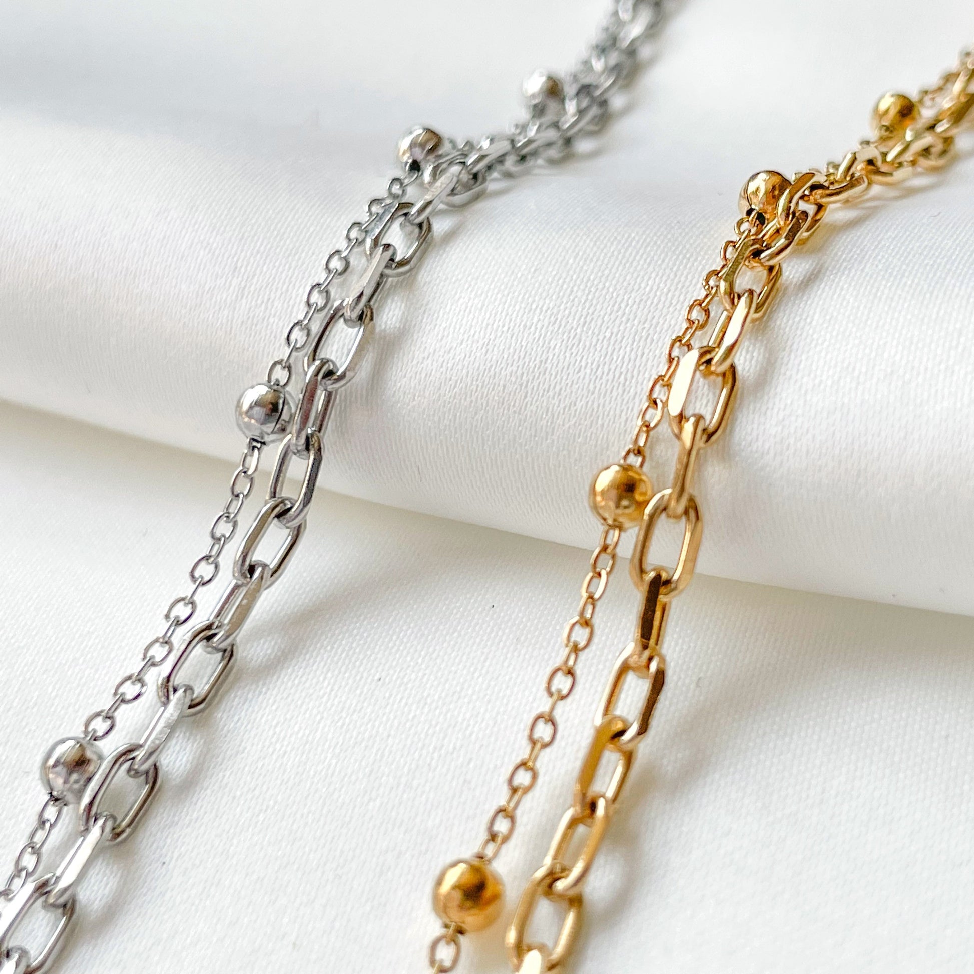 Two layered gold and silver chain bracelets on a white surface