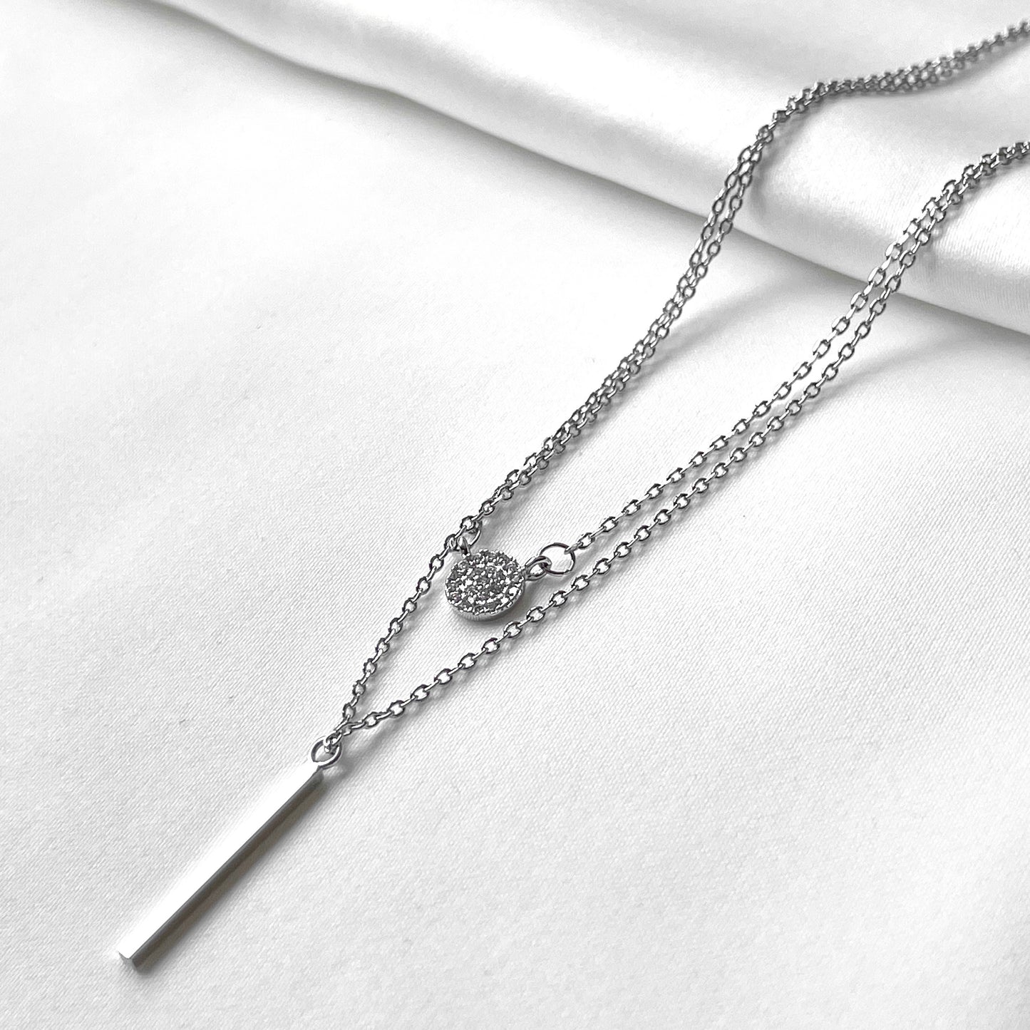 Silver necklace with disc charm and bar pendant on a white background