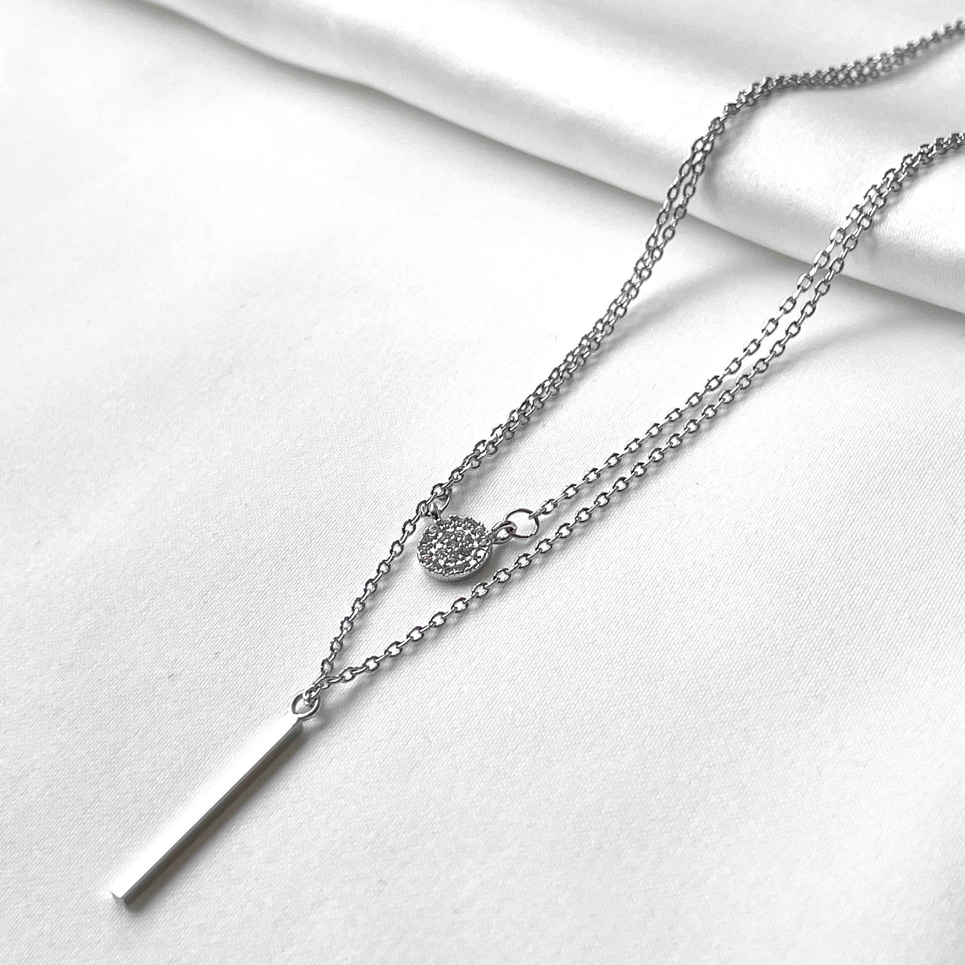 Silver necklace with disc charm and bar pendant on a white background