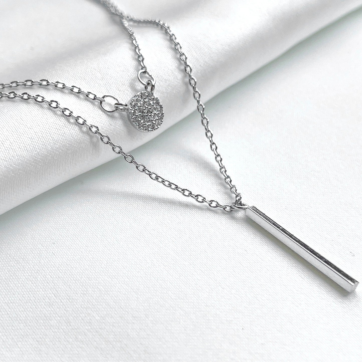 Layered silver necklace set on a white fabric background