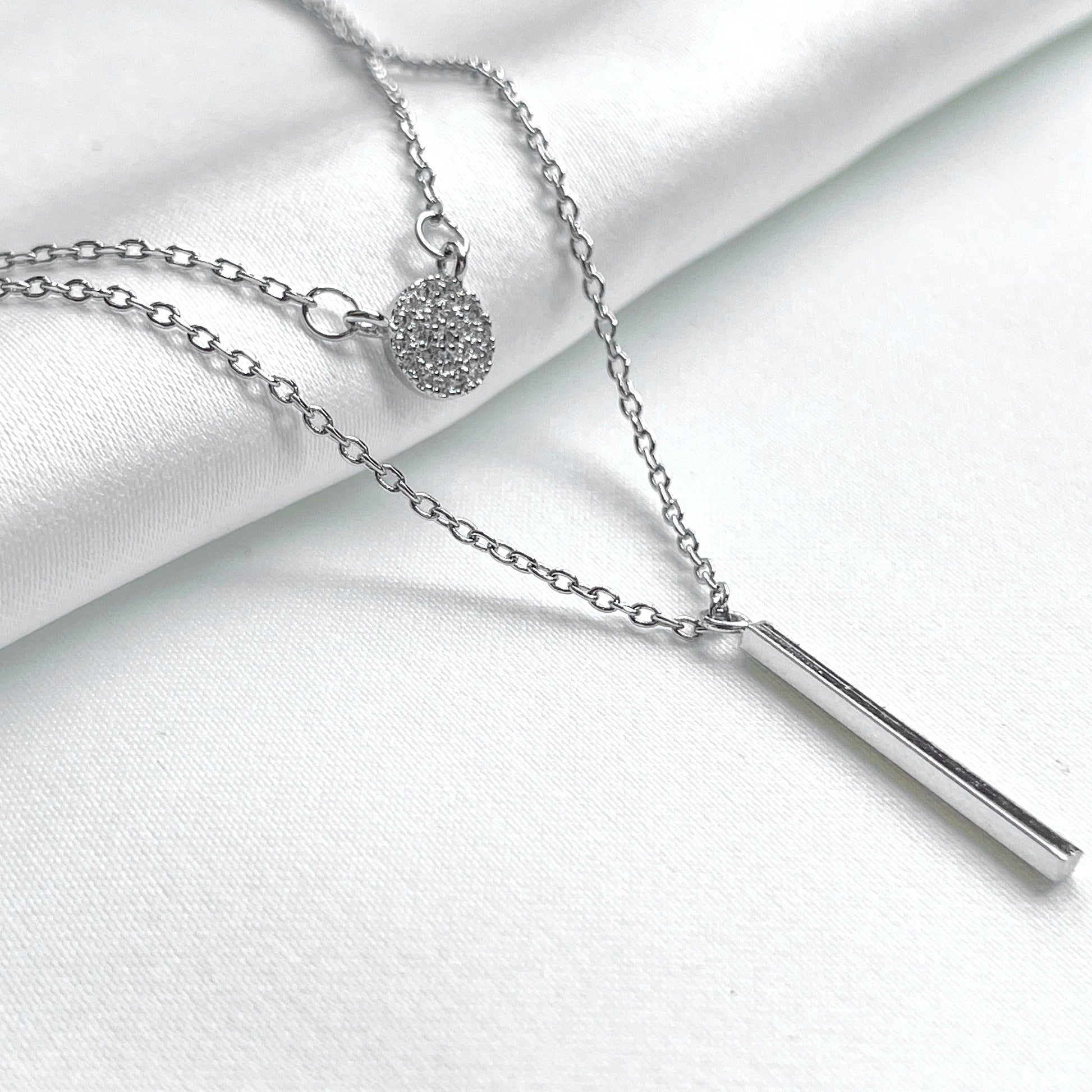 Layered silver necklace set on a white fabric background