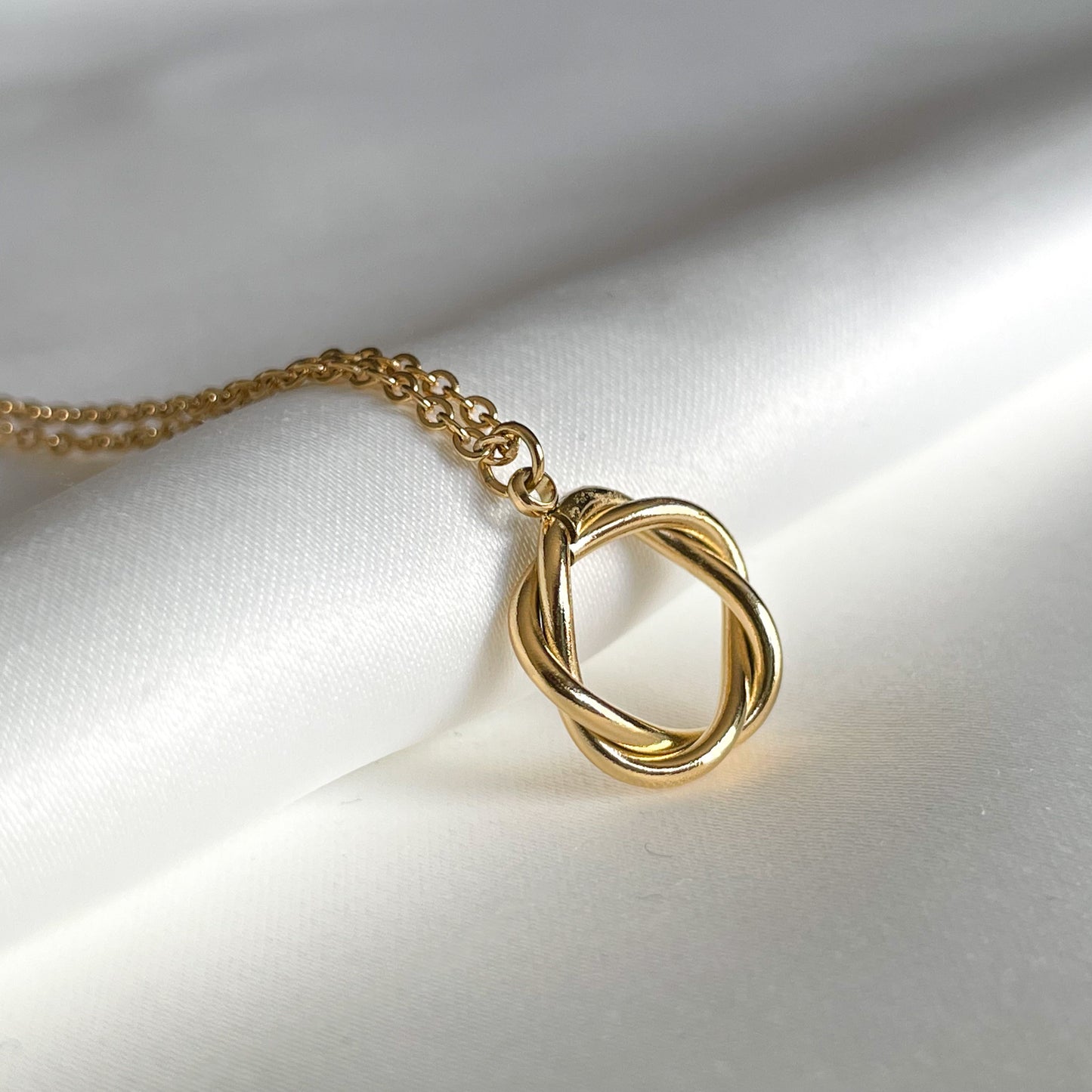 Gold necklace with a knot circle pendant on a white fabric background